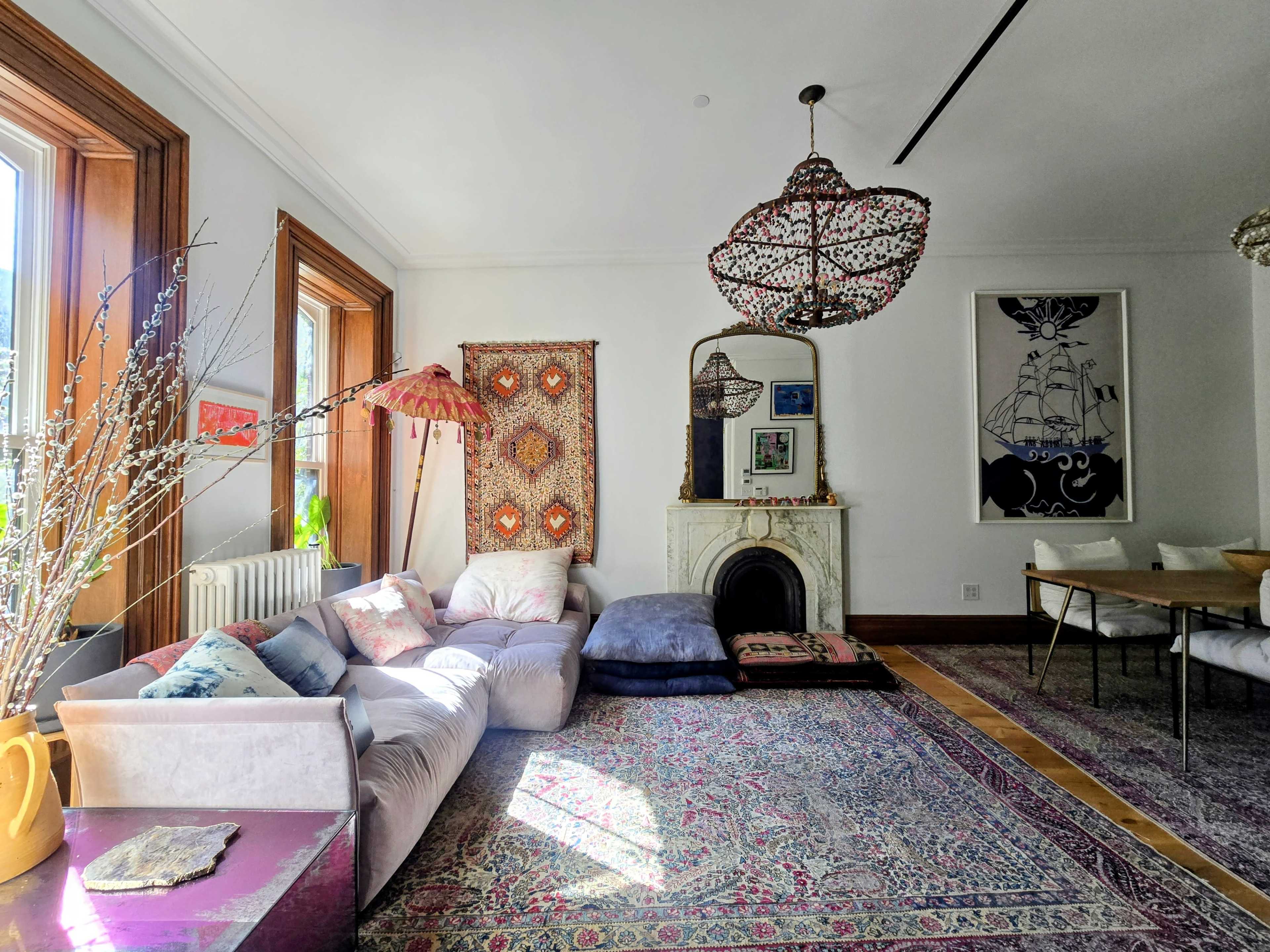 The living room features a large sofa, vibrant rugs, ornate light fixtures, and windows that allow natural light to fill the space.
