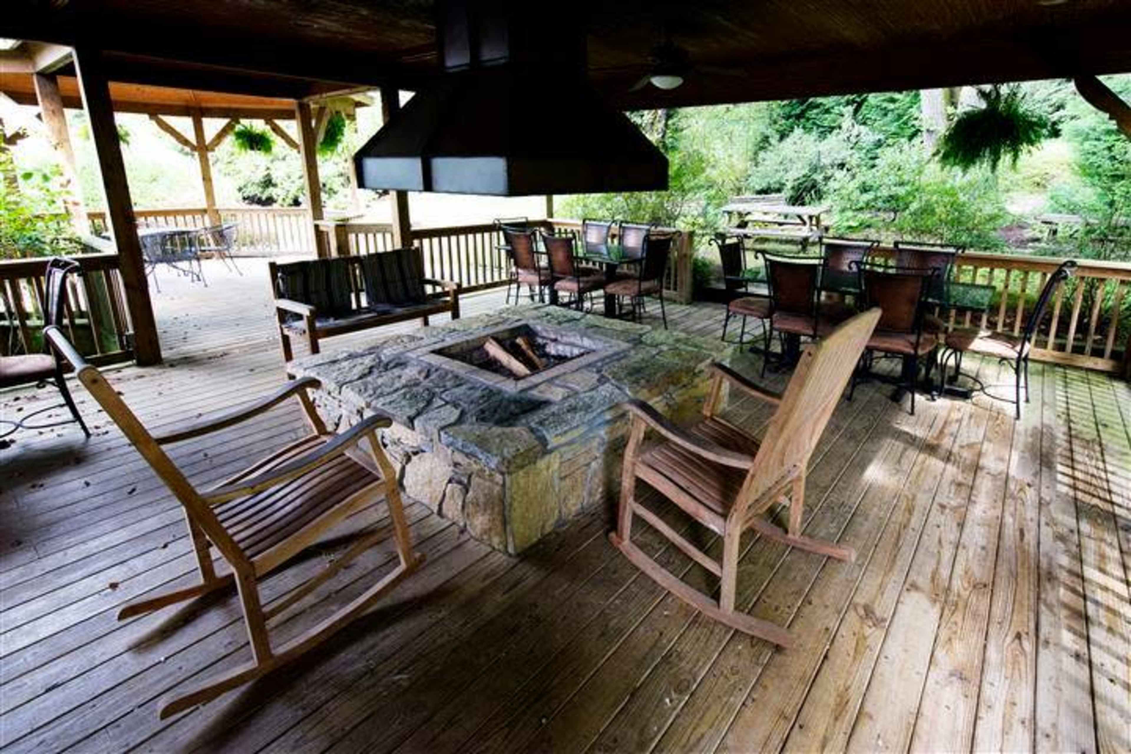 A covered outdoor deck featuring a stone fire pit surrounded by wooden rocking chairs and metal dining chairs.