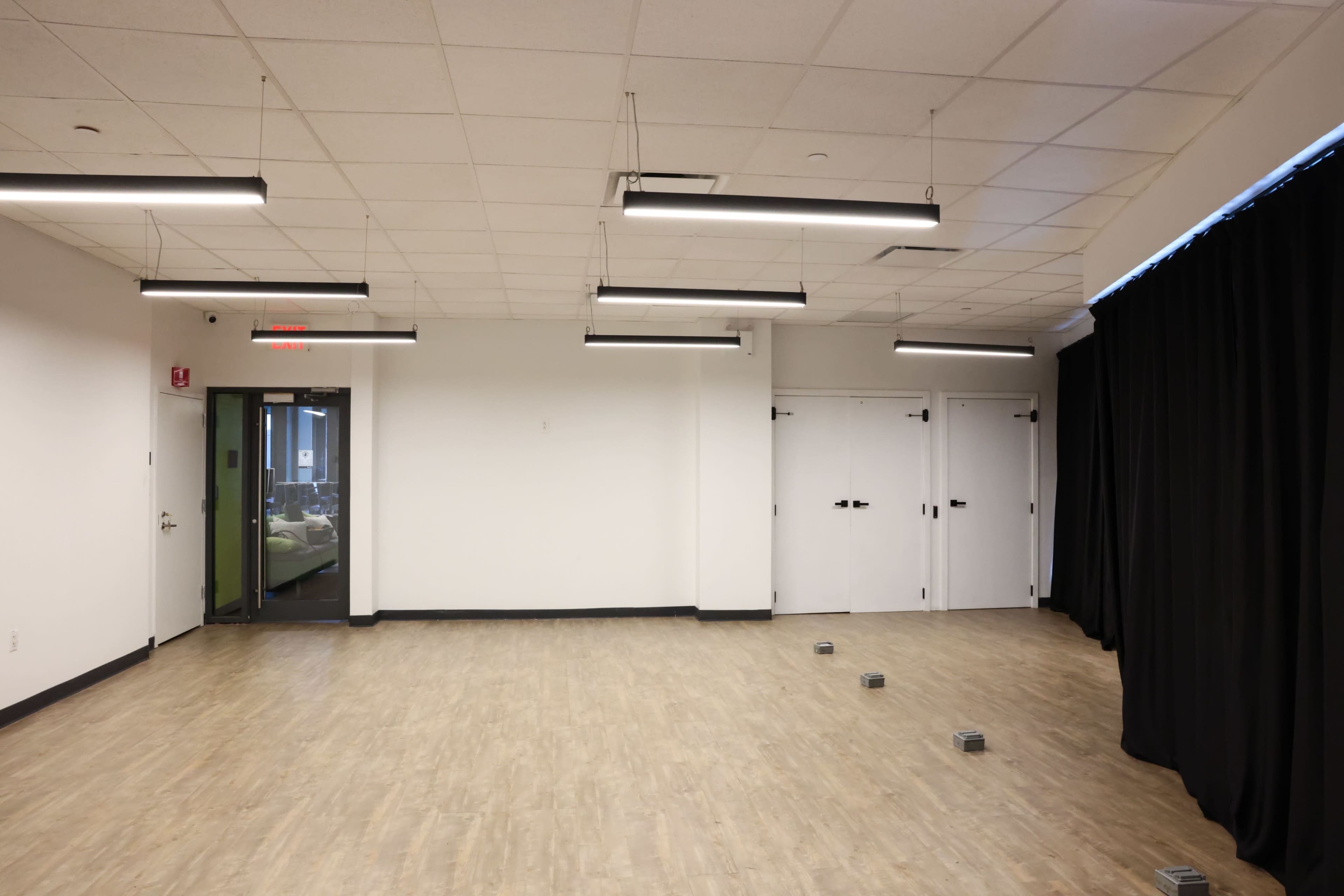 The image shows an empty room with a light-colored wooden floor, white walls, and several hanging light fixtures.
