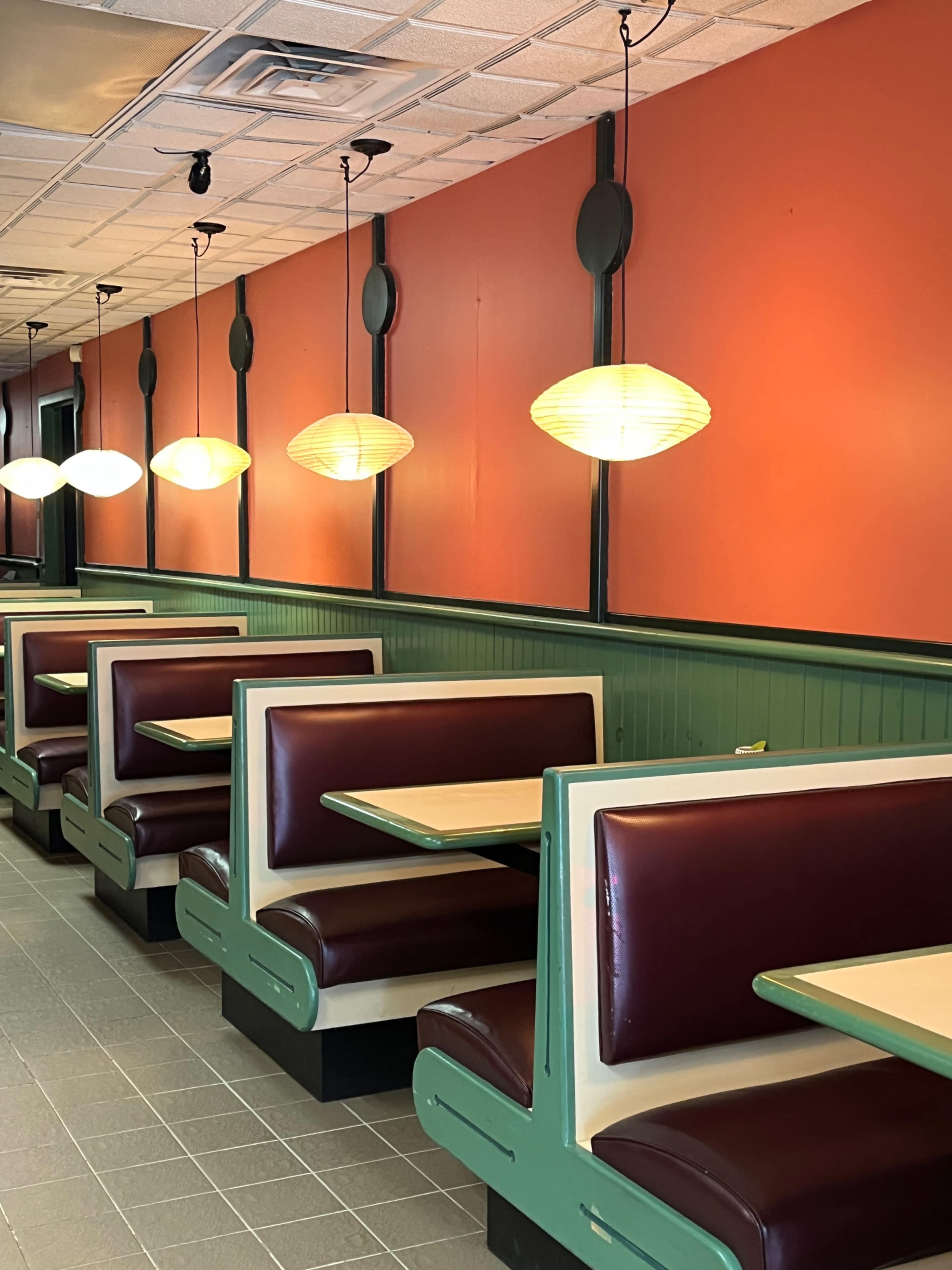 A row of brown-and-cream booths in a diner with orange walls and hanging pendant lights.