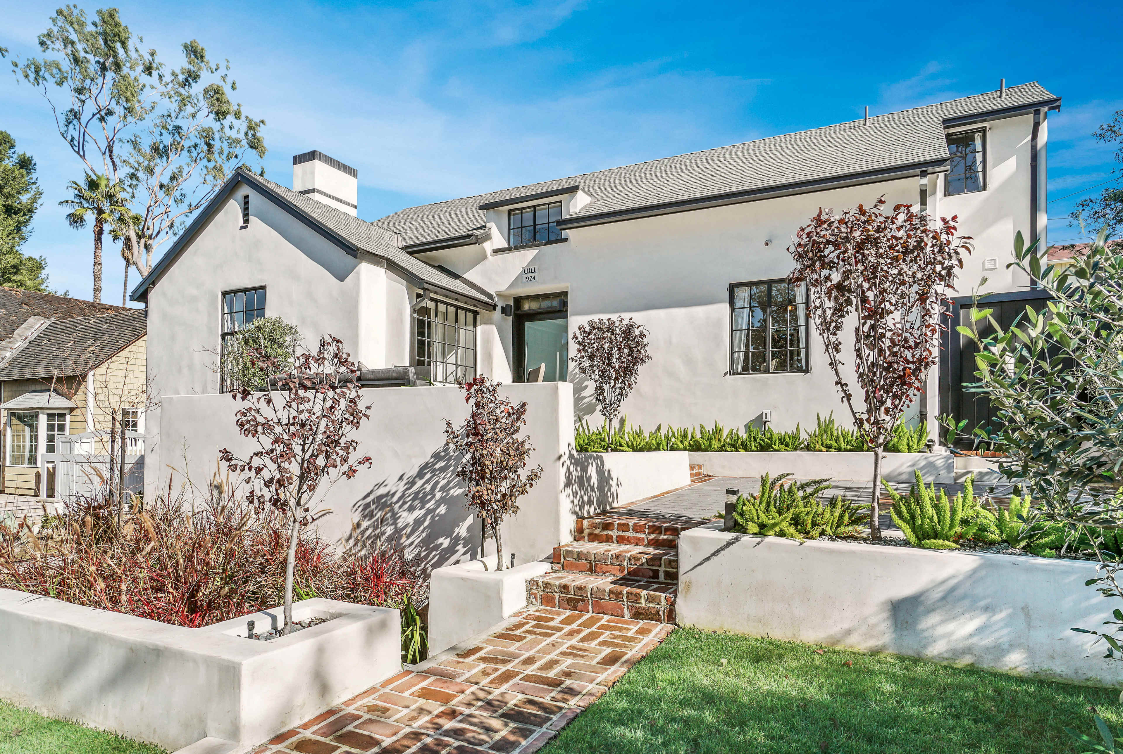 A modern, light-colored house features a landscaped front yard with steps leading up to the entrance.