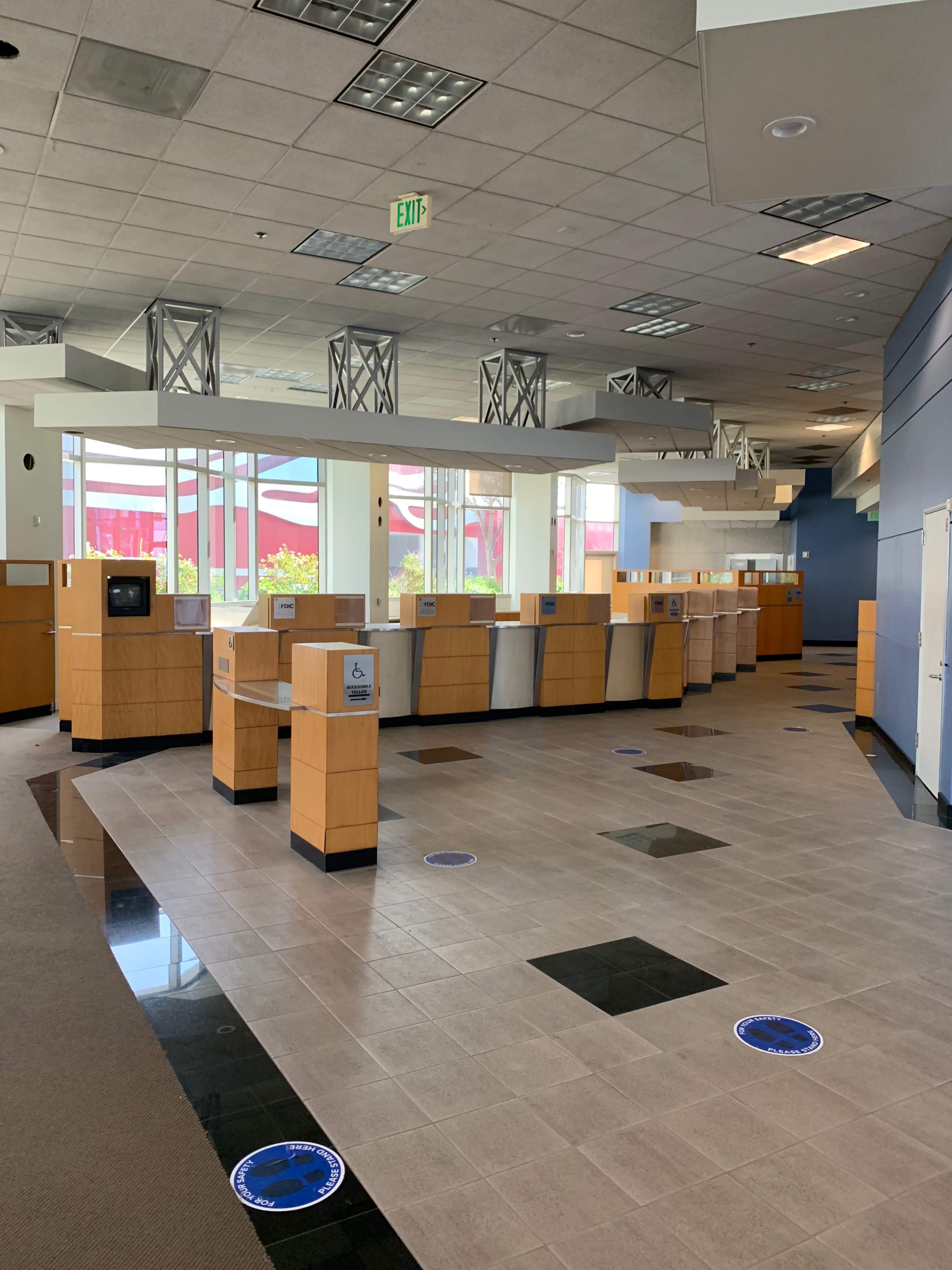 The image shows an empty bank interior with wooden service counters and tiled flooring.