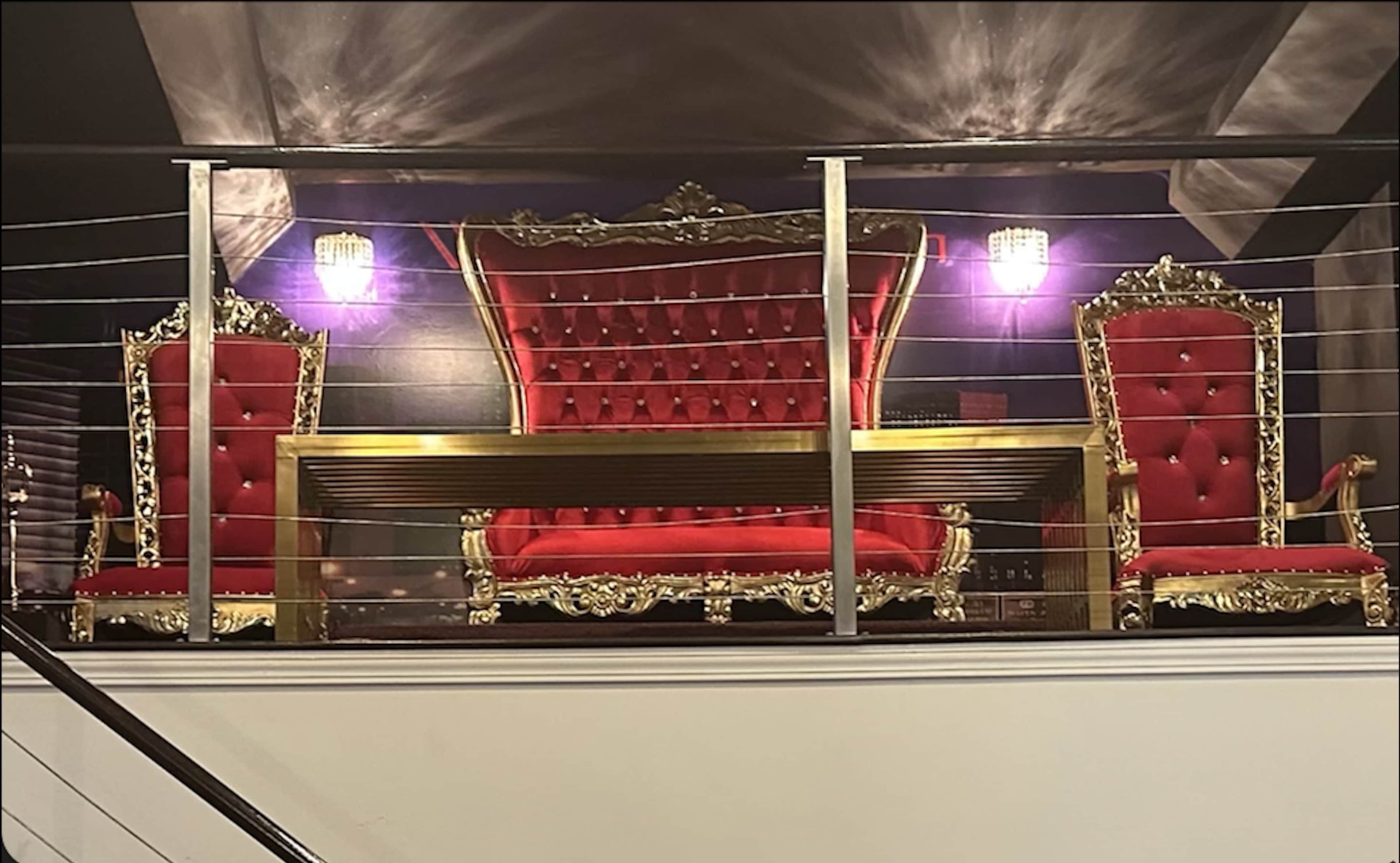 The image shows an ornate seating arrangement with a grand red and gold sofa flanked by two matching chairs, all set against a dark wall with purple lighting.
