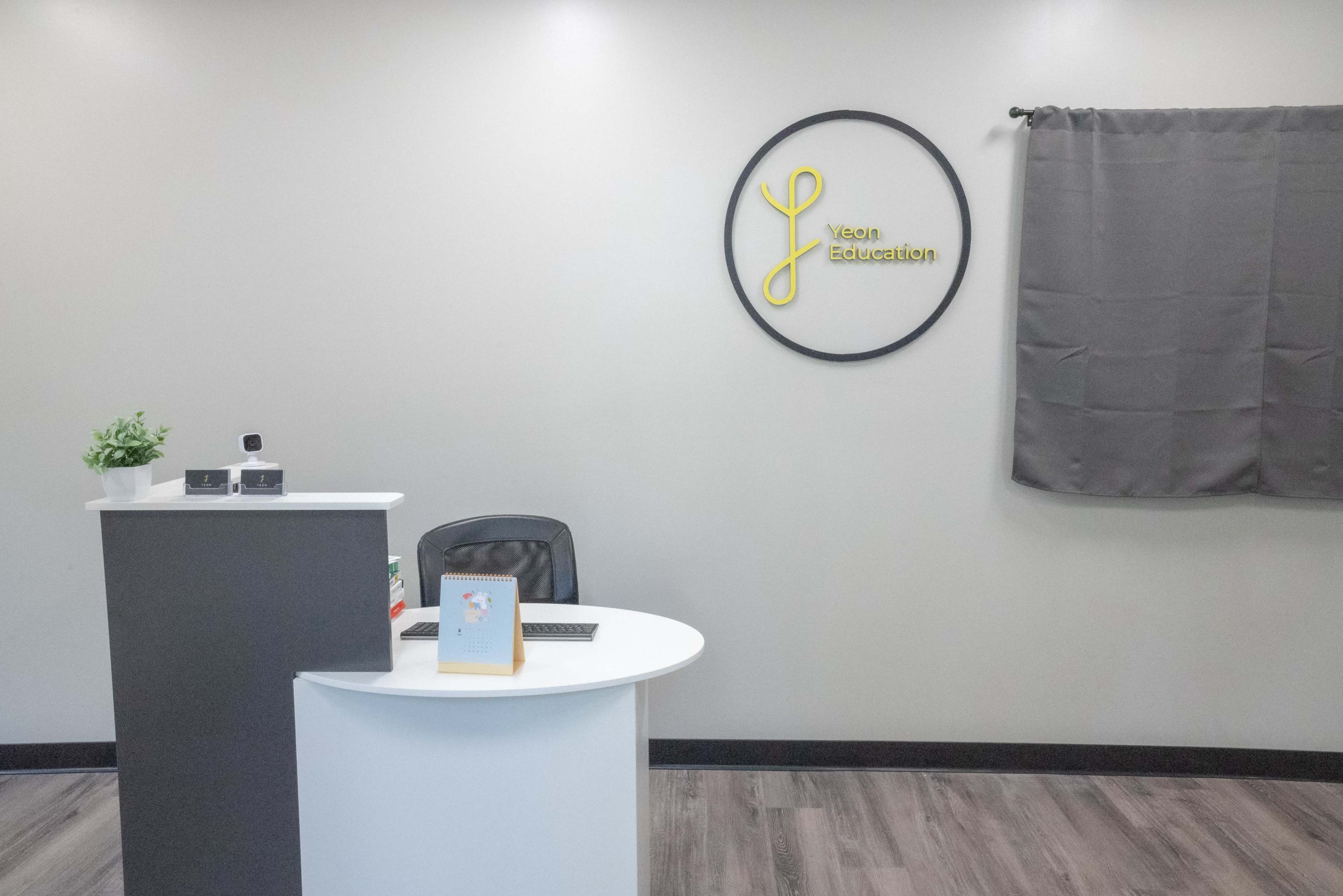 A reception area with a circular sign reading "Keen Education," a desk, a chair, and a gray curtain in the background.