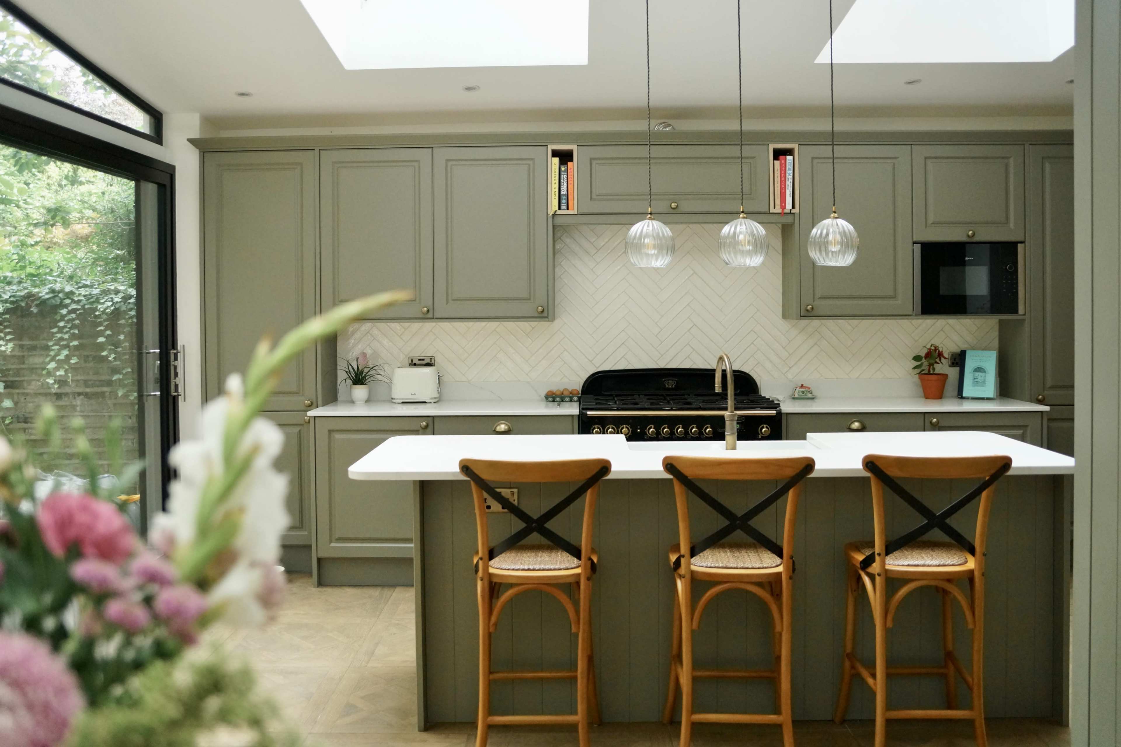 A modern kitchen with a central island, three bar stools, and a black range stove against a light-colored backsplash.