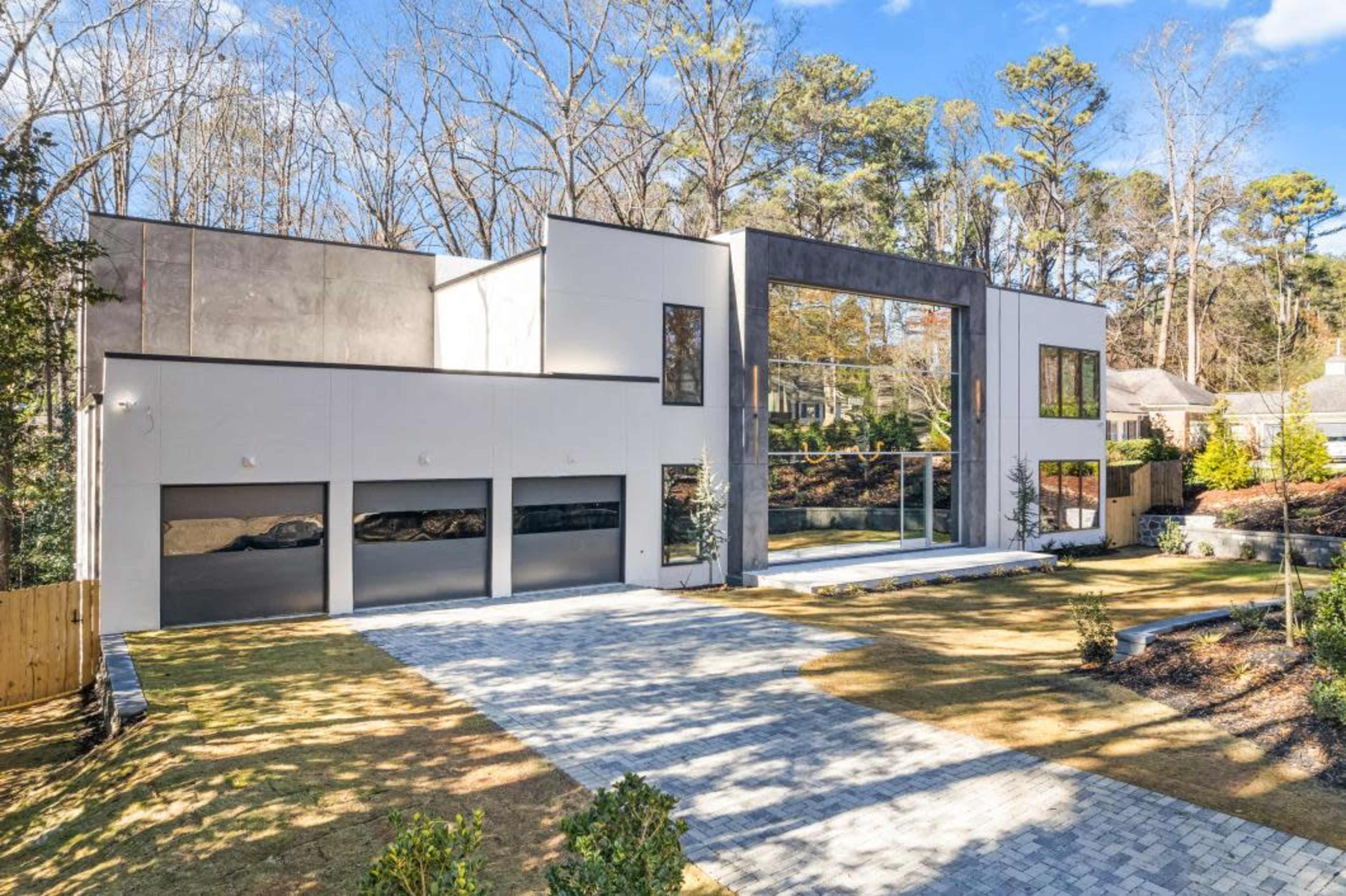 The image shows a modern two-story house with large glass windows and a three-car garage, surrounded by a landscaped yard.