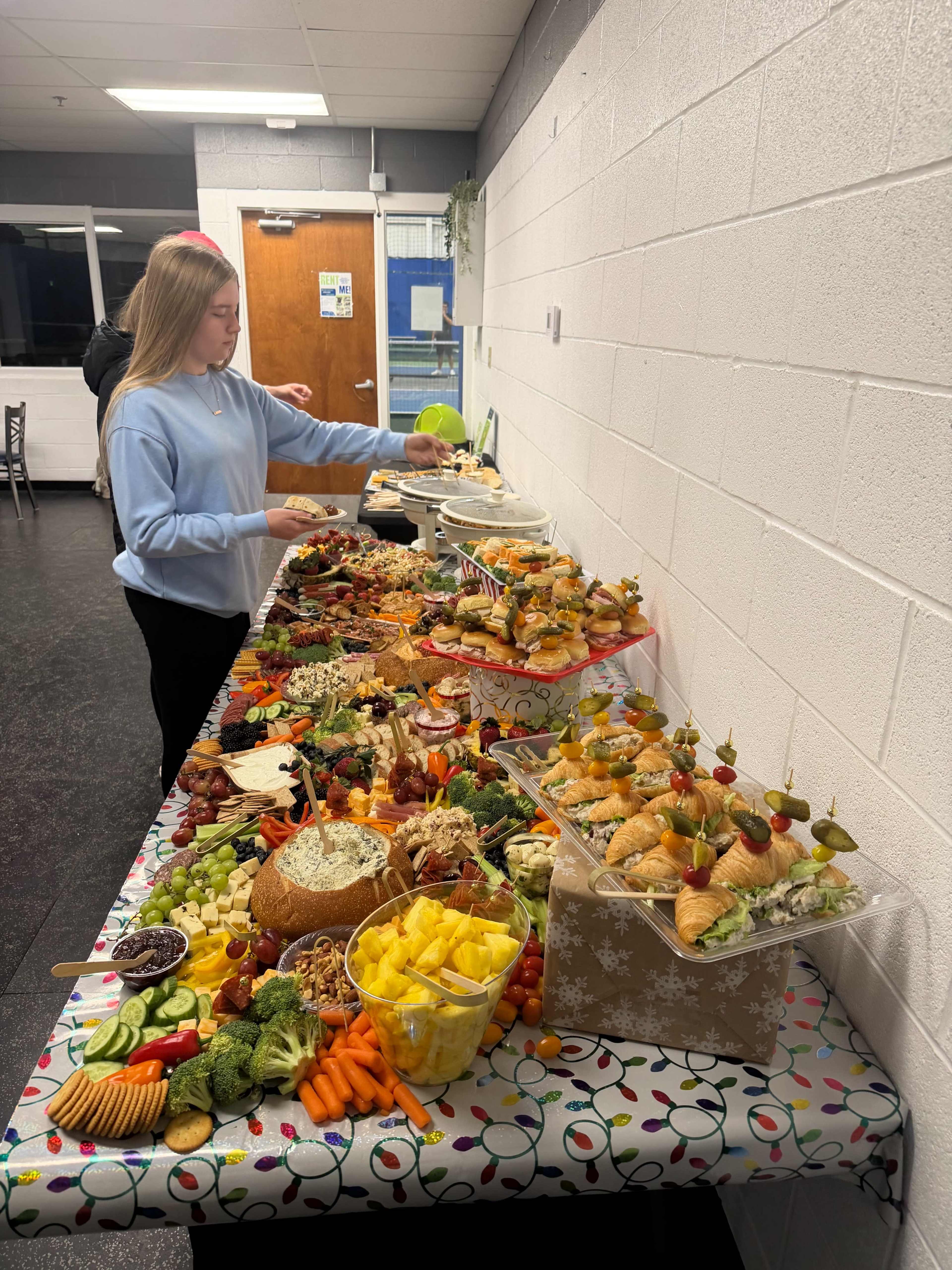 A young woman is serving food from a large buffet table filled with a variety of fruits, vegetables, meats, and desserts.