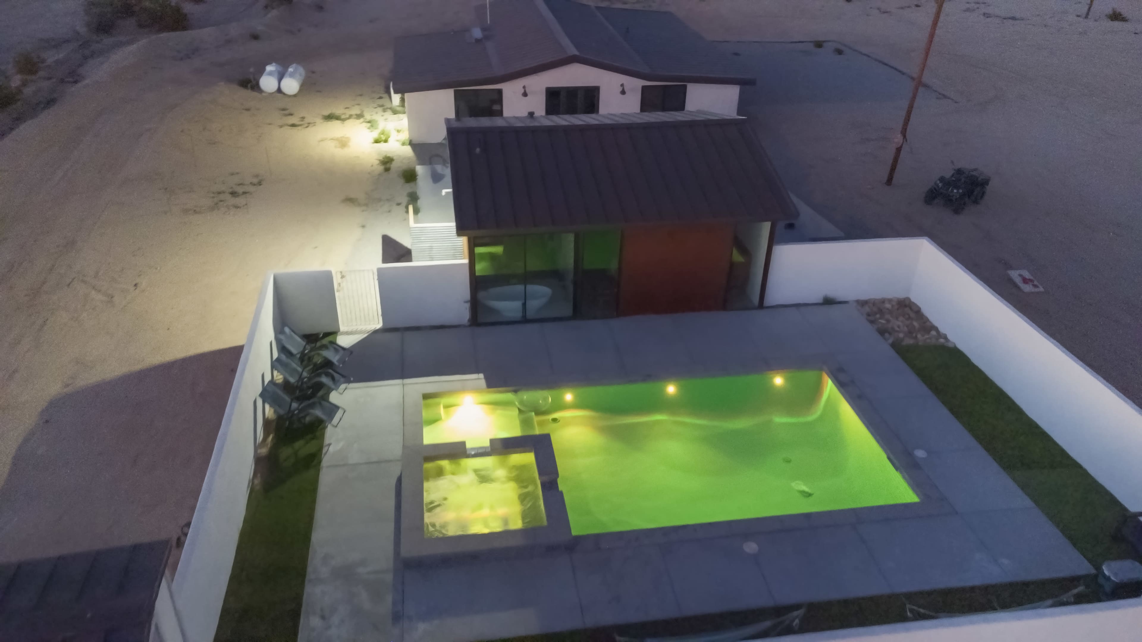 A modern house with a swimming pool illuminated at night, surrounded by a desert landscape.