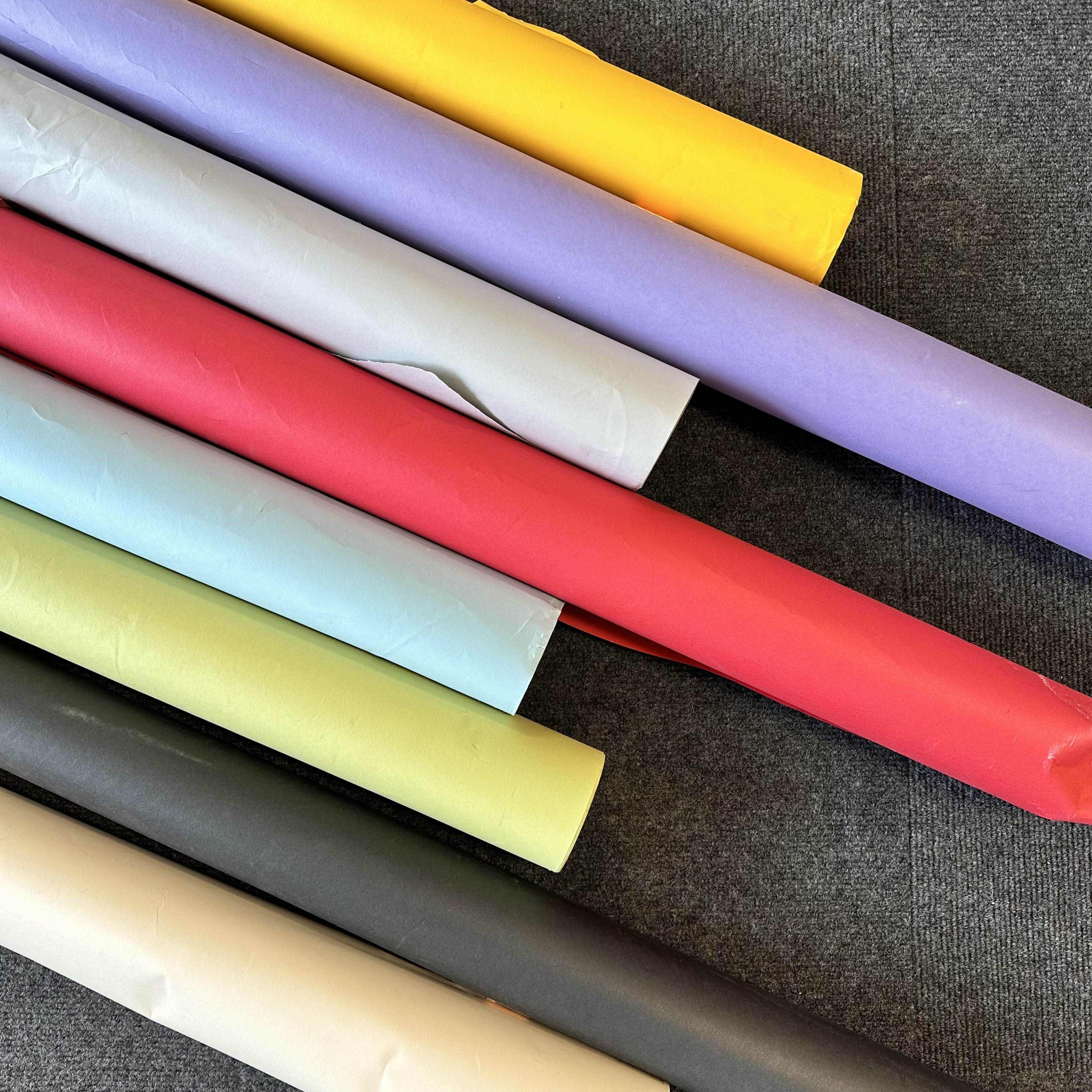 A collection of rolled sheets of colored paper arranged in a stack on a gray surface.