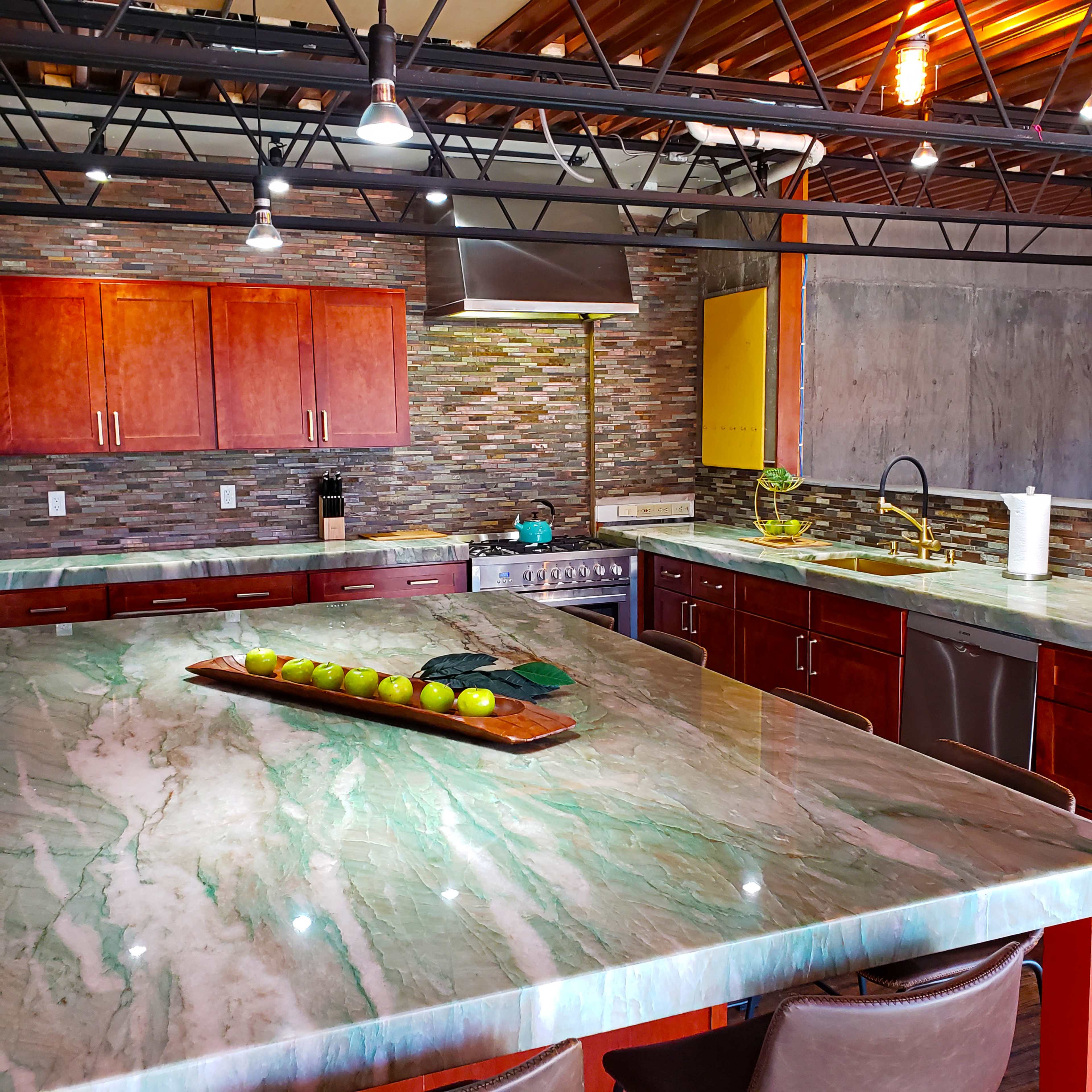 The kitchen features wooden cabinetry, a large marble island with green apples, and modern appliances against a stone backsplash.