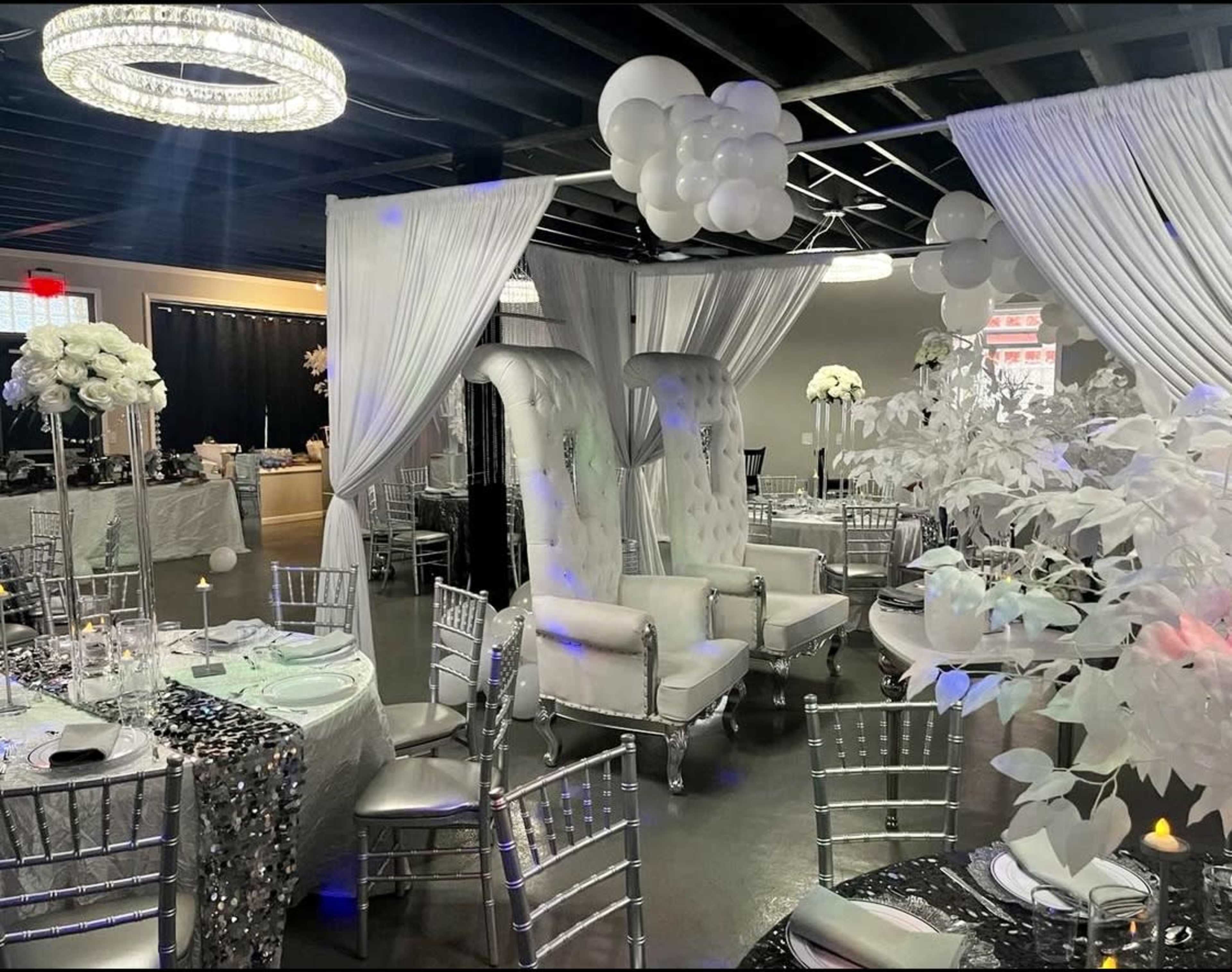 A decorated event space with elegantly set round tables, white drapery, and plush seating arranged for a formal gathering.