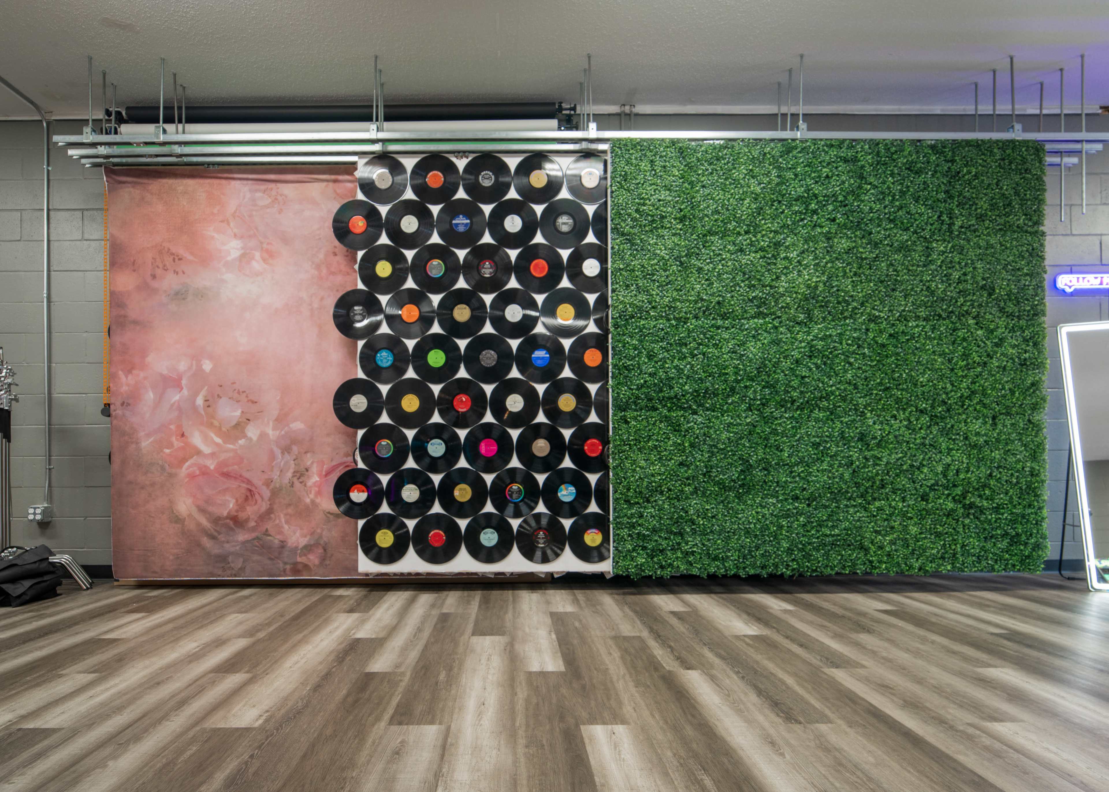 A wall divided into two sections: one adorned with a textured pink surface and the other decorated with black vinyl records arranged in a grid, alongside a green vertical garden panel.