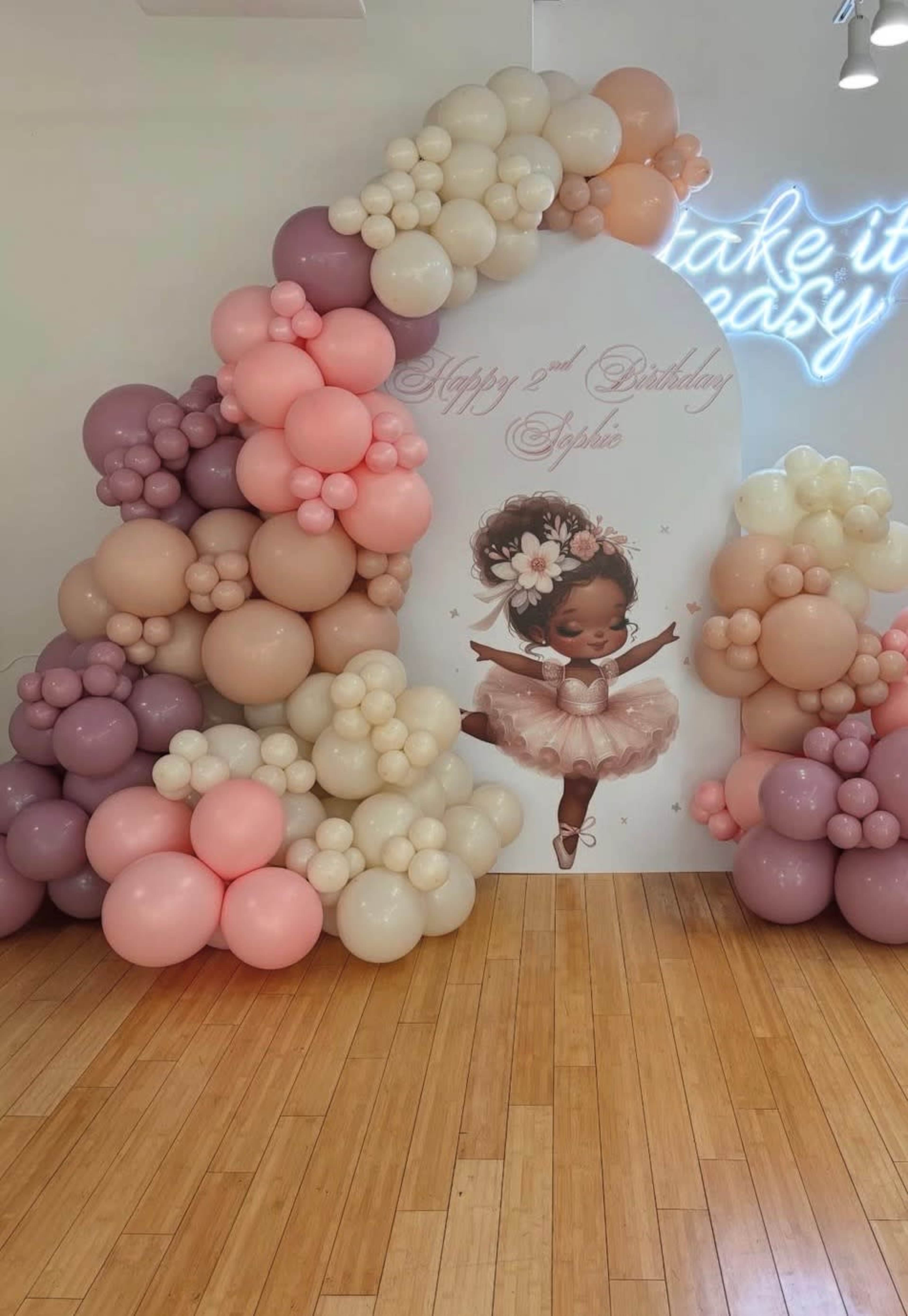 The image shows a colorful balloon arch featuring various shades of pink, purple, and cream, alongside a backdrop that reads "Happy 2nd Birthday Sophie" with an illustration of a young girl in a ballet pose.