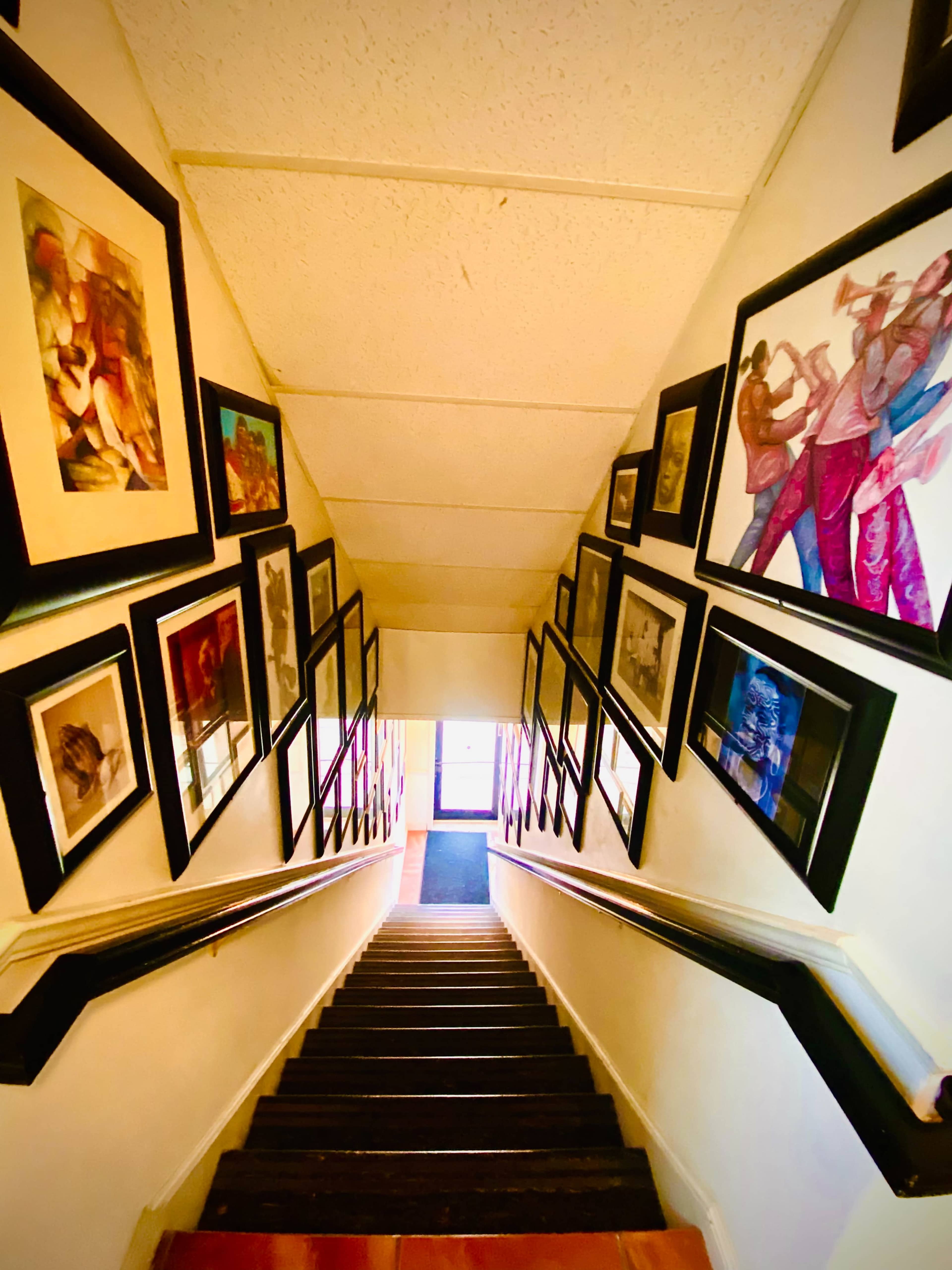 A staircase lined with framed artwork on the walls, leading down to a door at the bottom.