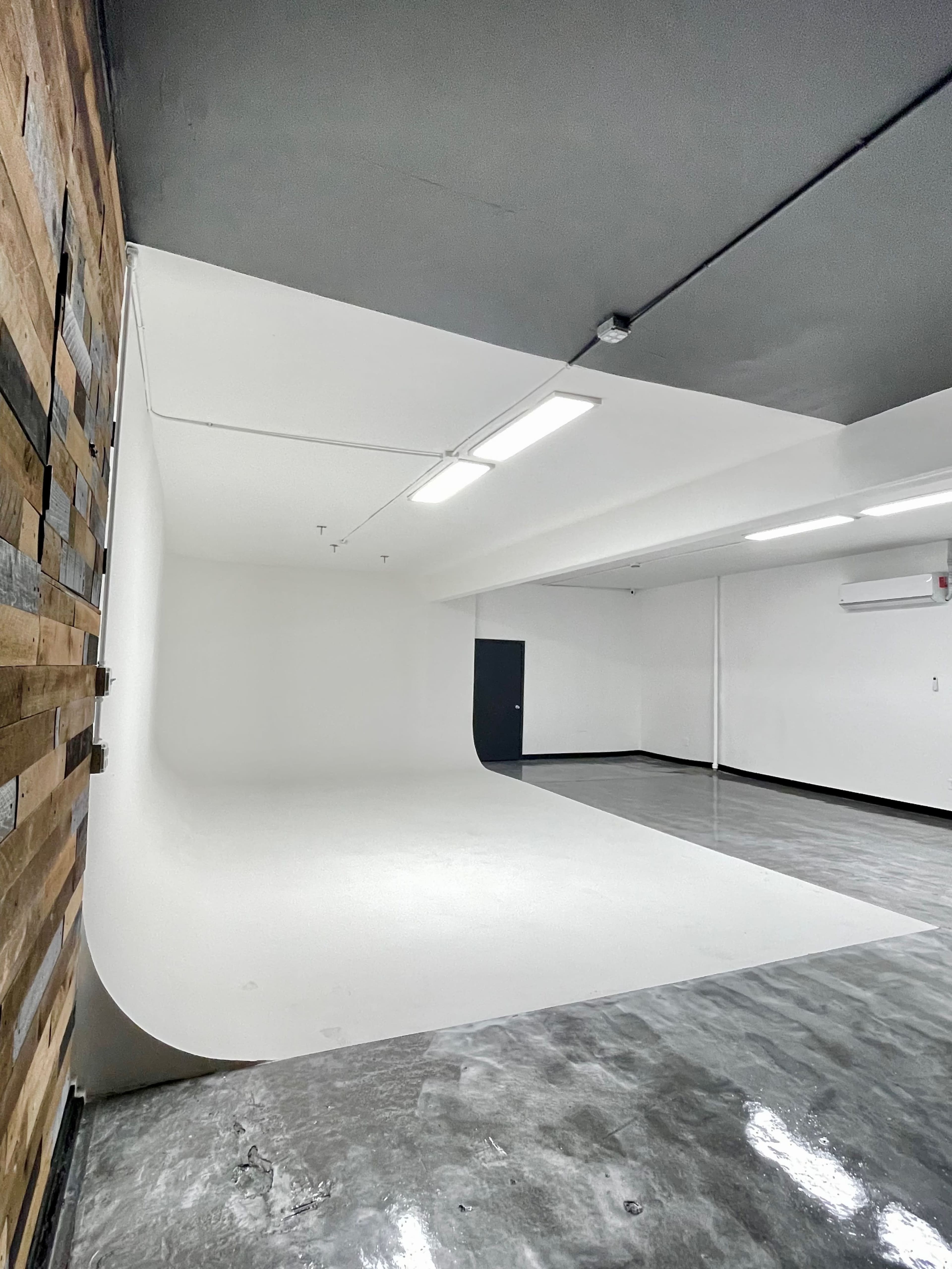 The image shows a spacious studio with a white curved backdrop, polished concrete floors, and a wooden accent wall.