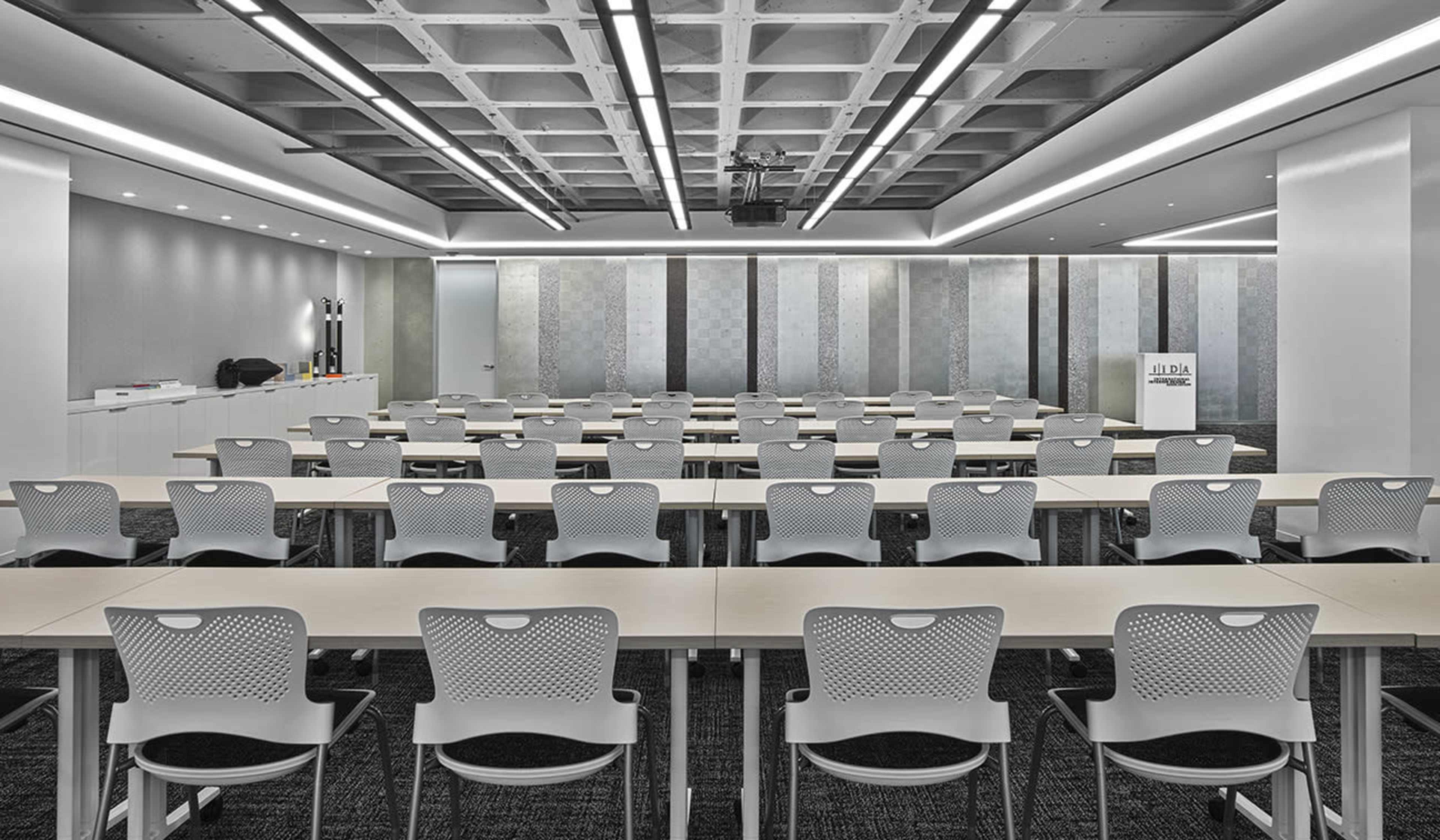 A modern conference room arranged with multiple rows of tables and chairs, designed for meetings or presentations.