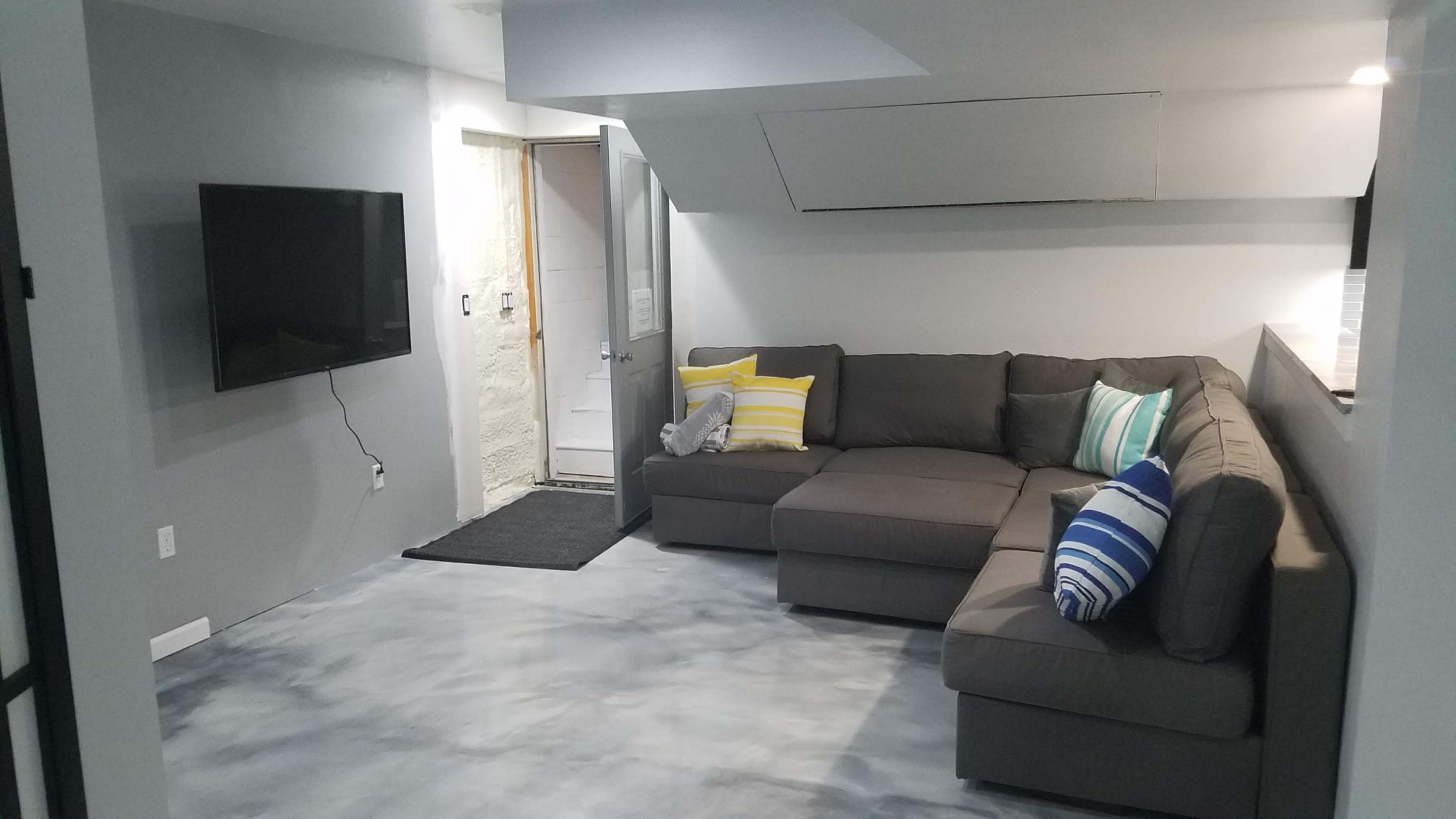 A modern, gray living room with a sectional sofa, a wall-mounted TV, and a door leading to another space.