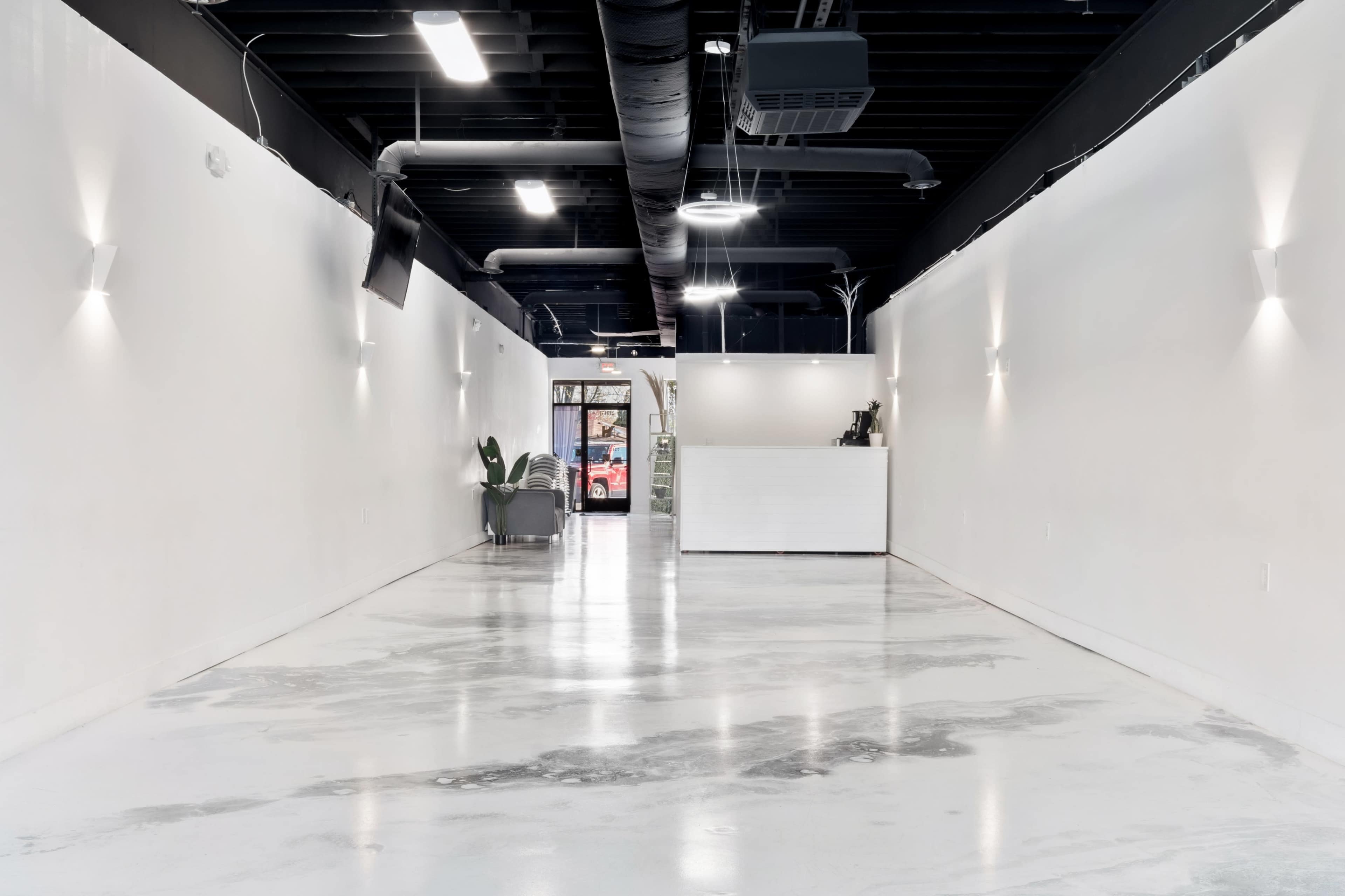 The image shows a spacious, modern interior of a commercial hallway leading to a reception area with a white counter and clean, polished concrete floors.