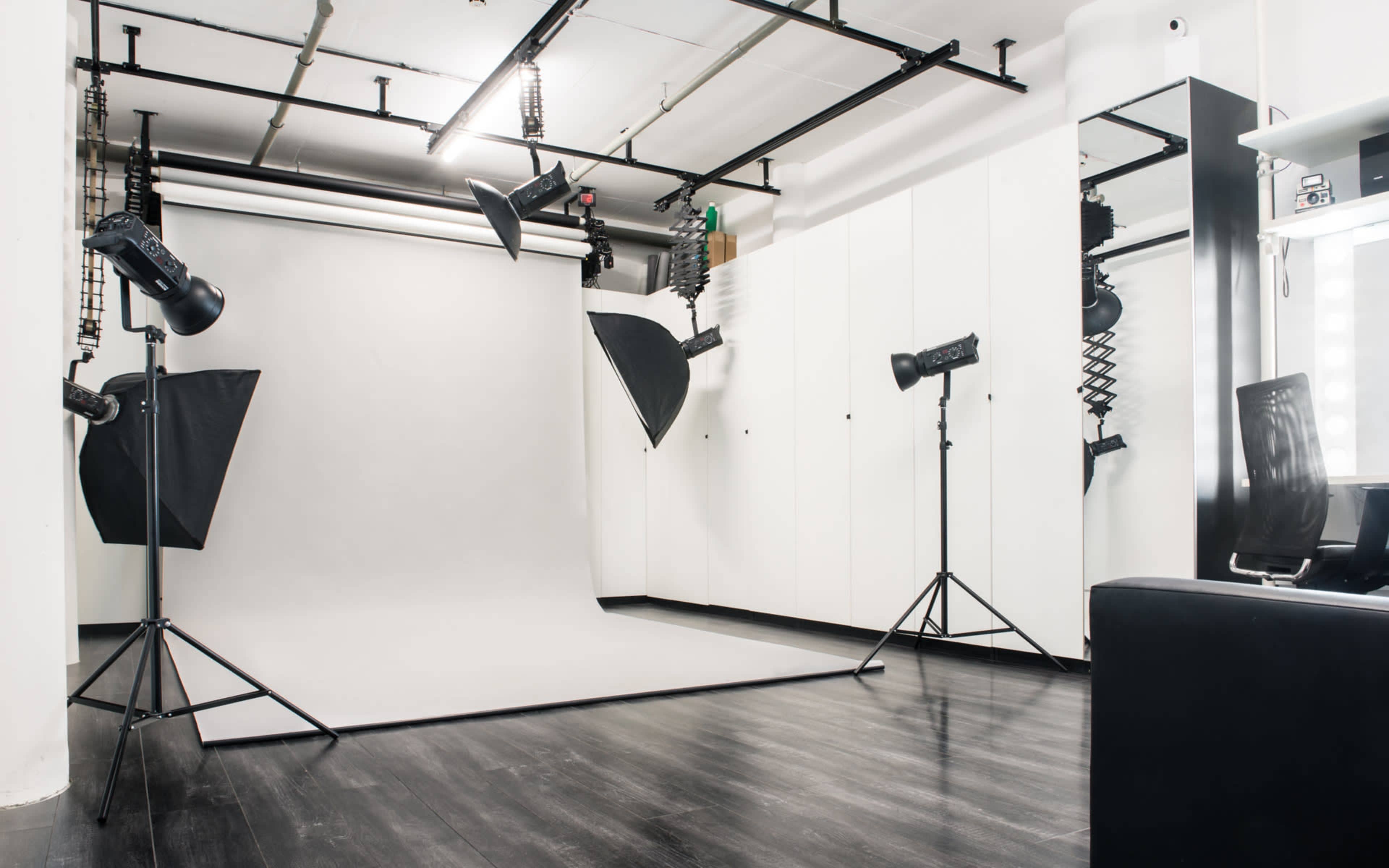 A photography studio with a gray backdrop, lighting equipment, and a black chair.