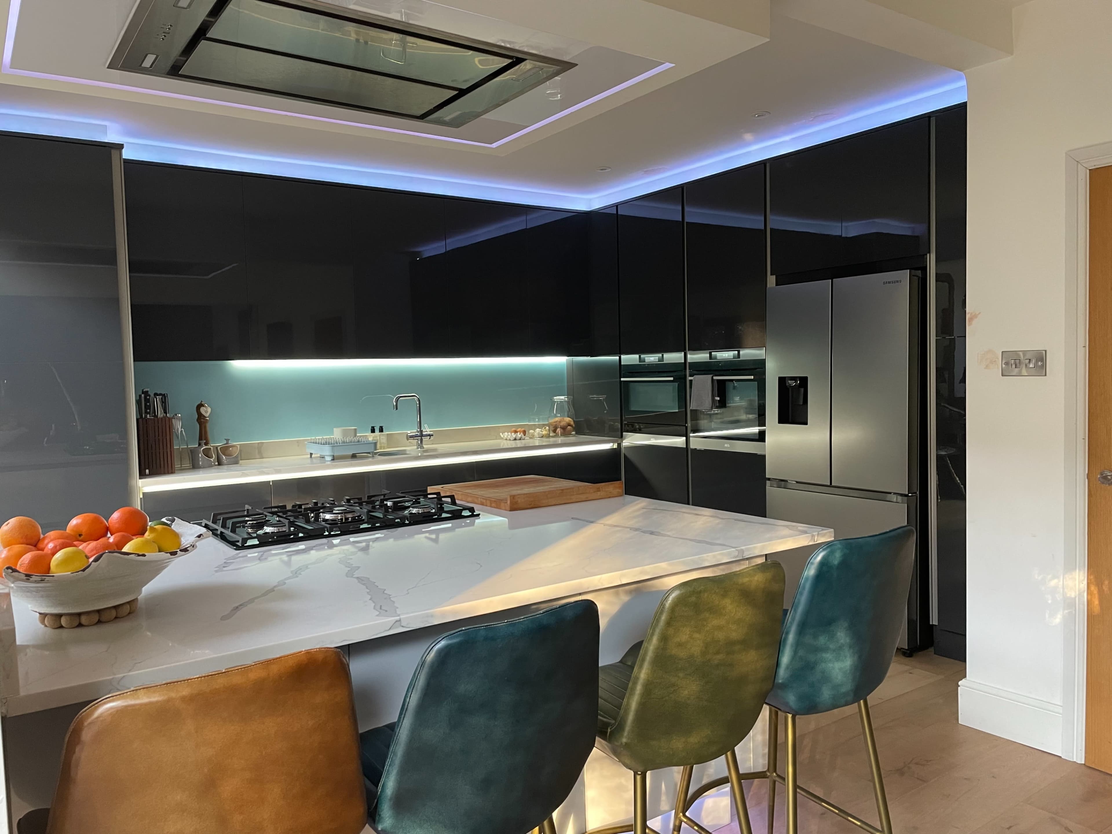 A modern kitchen features a central island with bar stools, sleek black cabinetry, and a large gas cooktop.