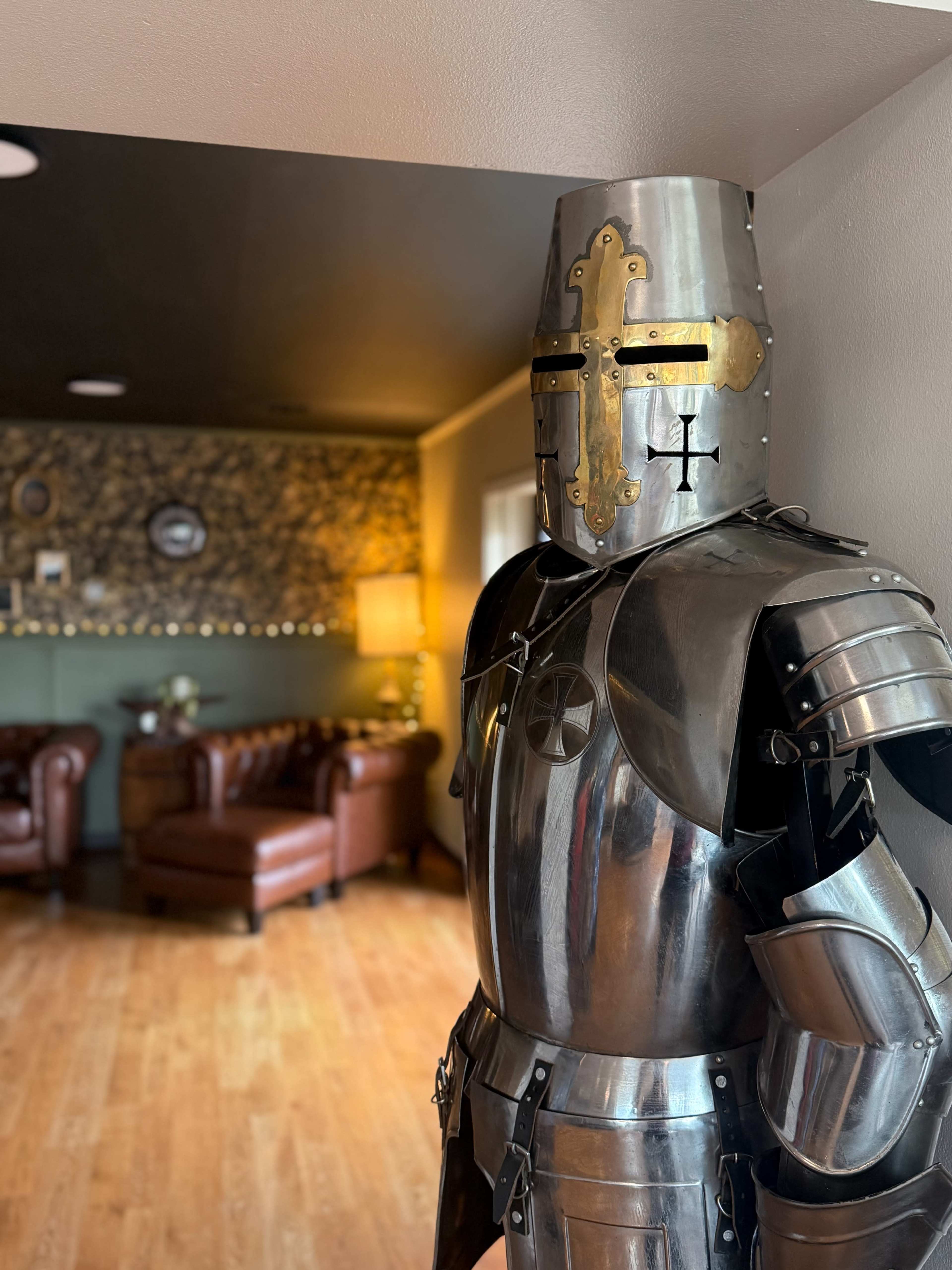 A suit of medieval armor stands in a doorway, with a cozy room featuring leather couches visible in the background.