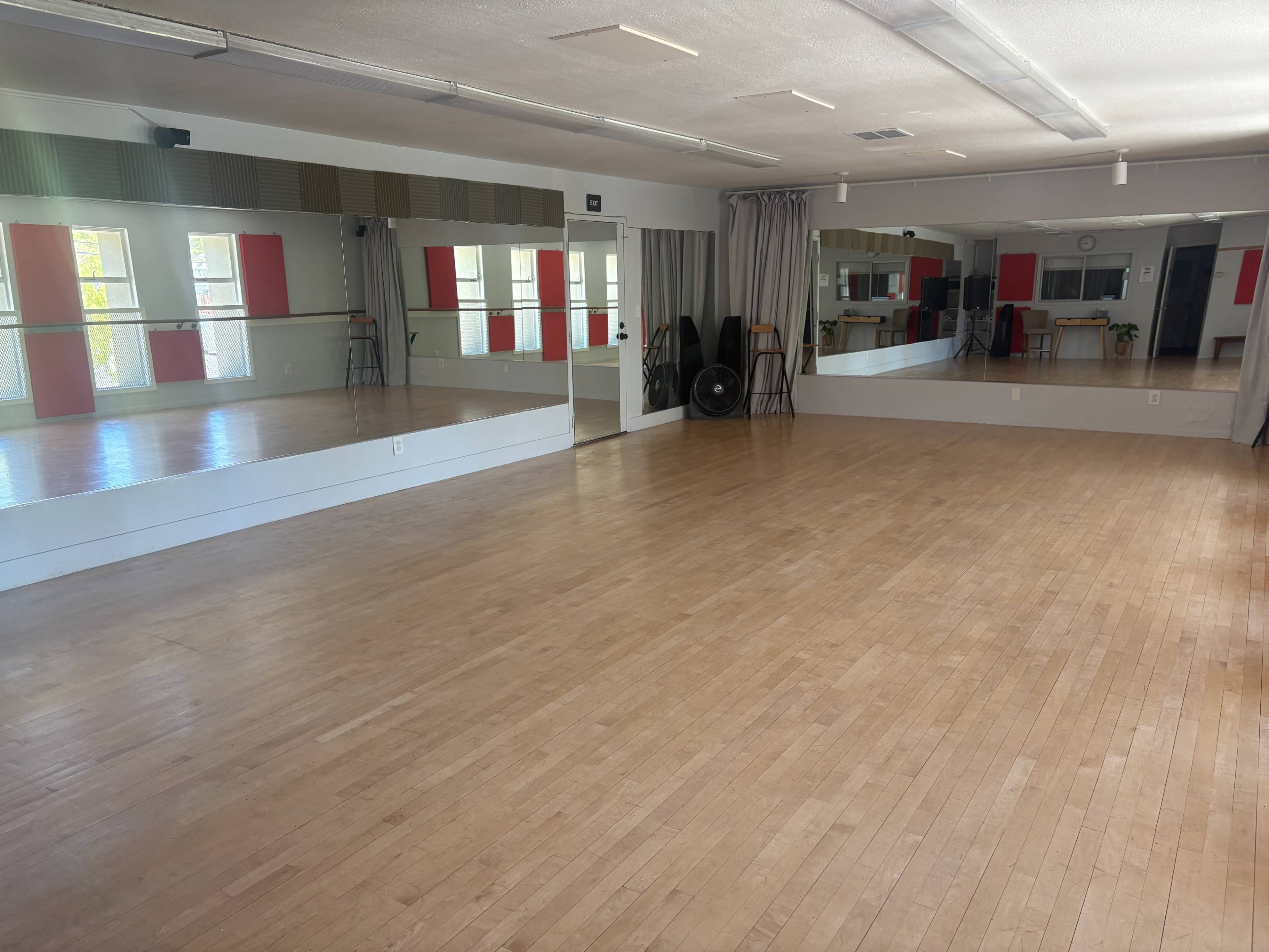 The image shows a spacious, empty dance studio with wooden floors and large mirrors on one wall.