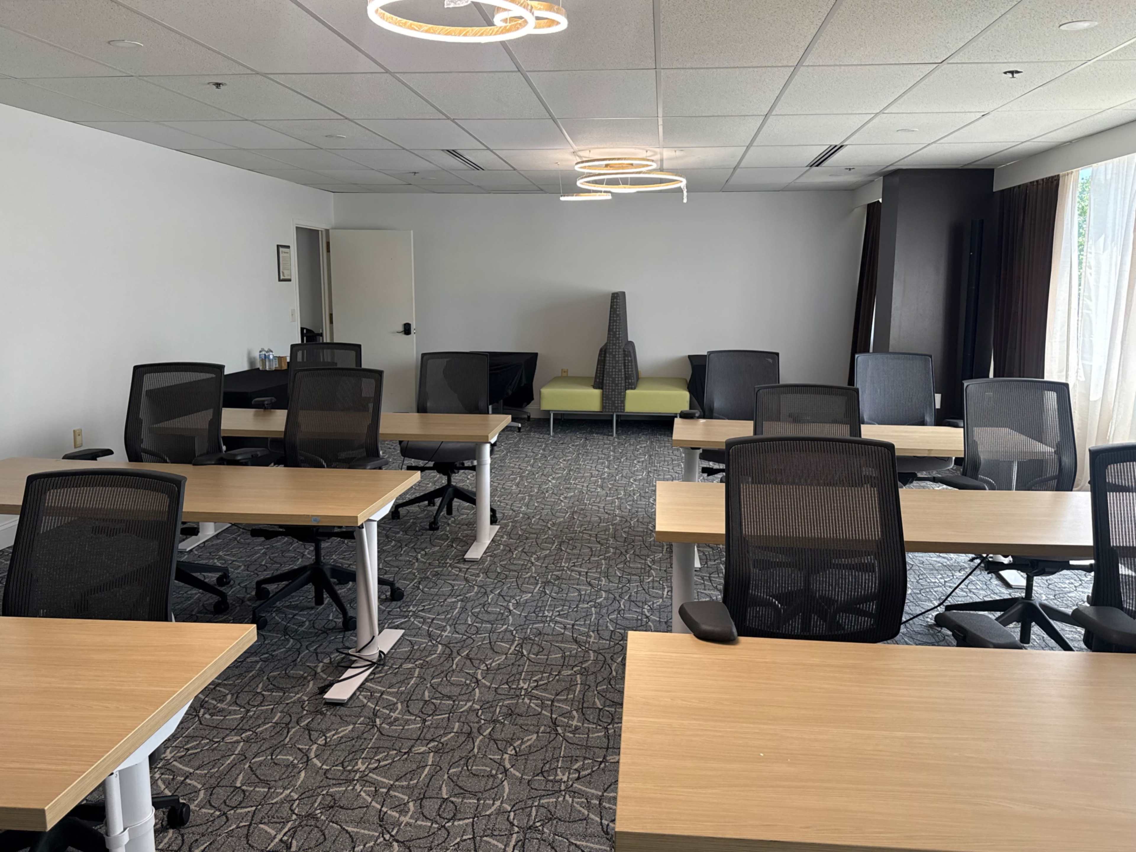 The image shows a spacious, empty conference room with several tables and ergonomic chairs arranged neatly, and a green couch positioned against one wall.