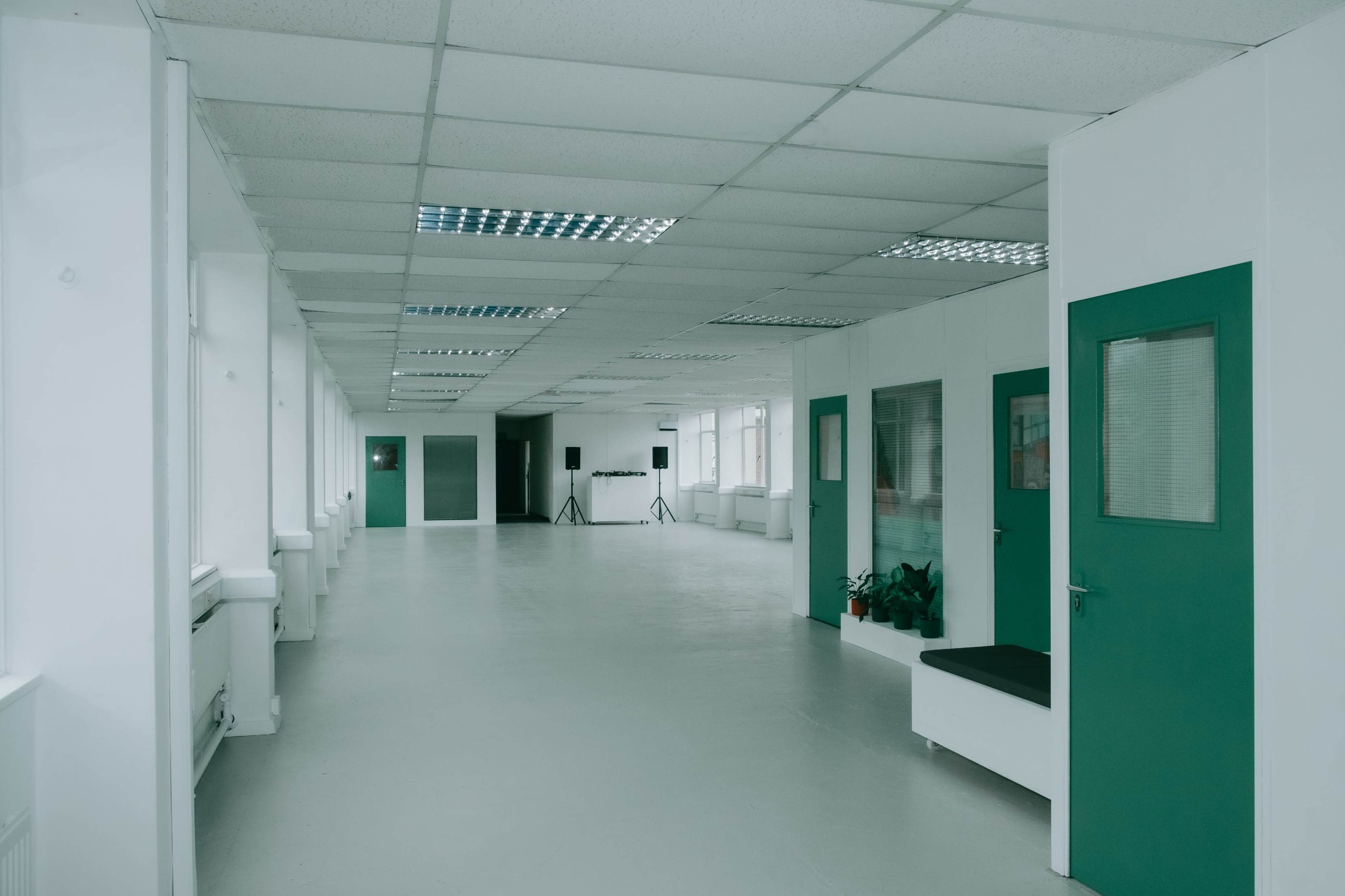 A long, empty hallway in a brightly lit building features green doors and a minimalist design.
