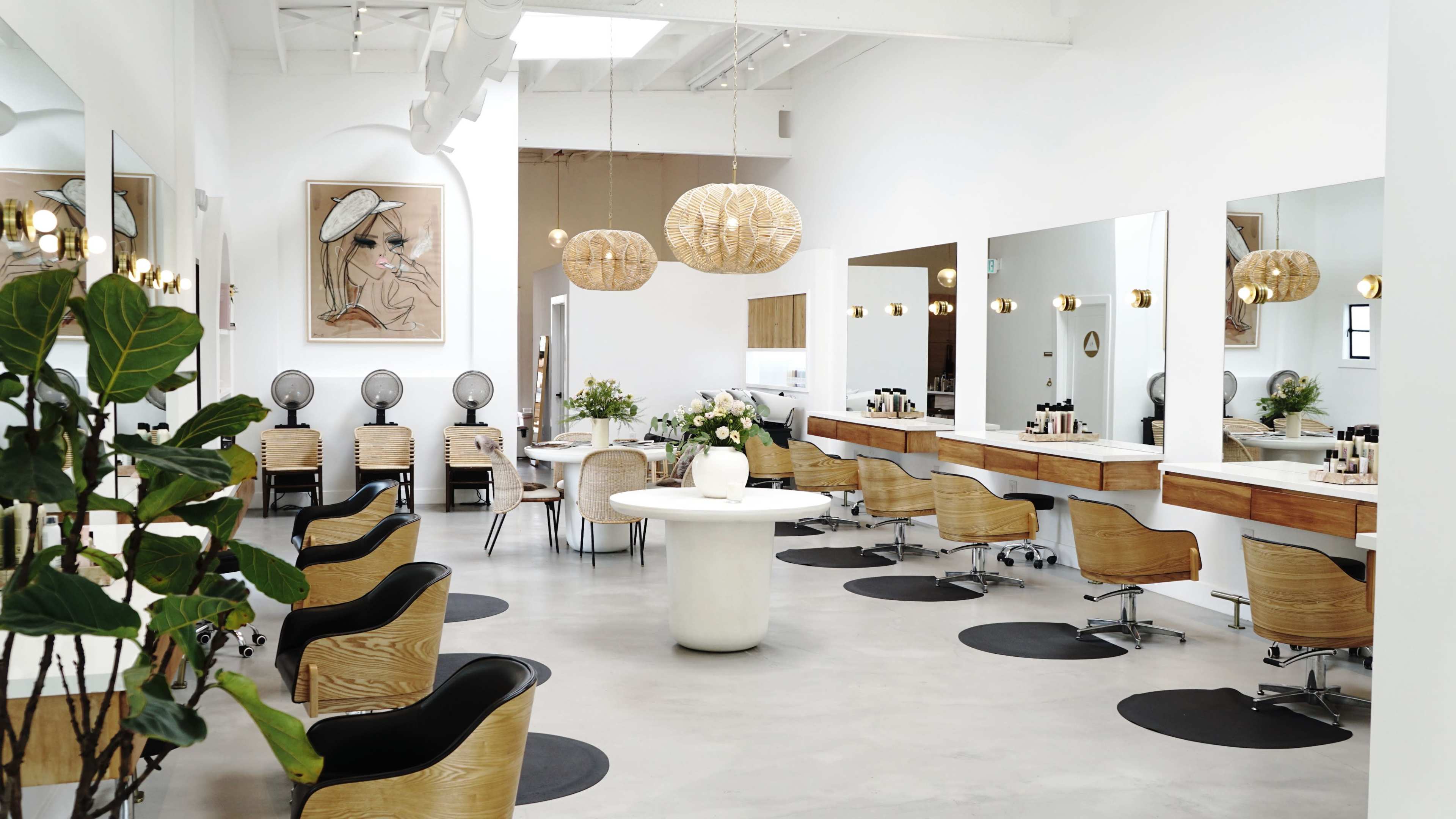 The interior of a modern salon features sleek wooden furniture, large mirrors, and stylish light fixtures, all set against a minimalist white backdrop.