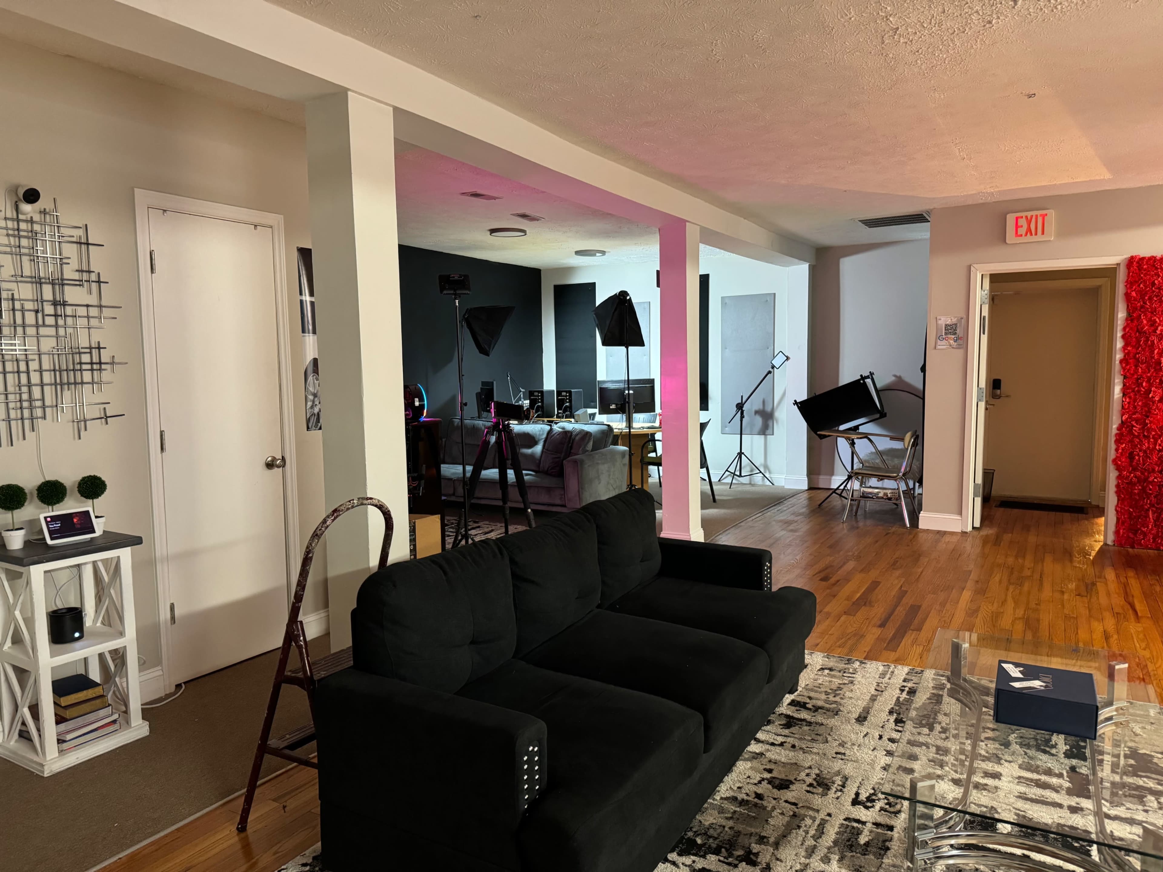 A living room area with a black couch, a patterned rug, and studio lighting equipment set up in the background.
