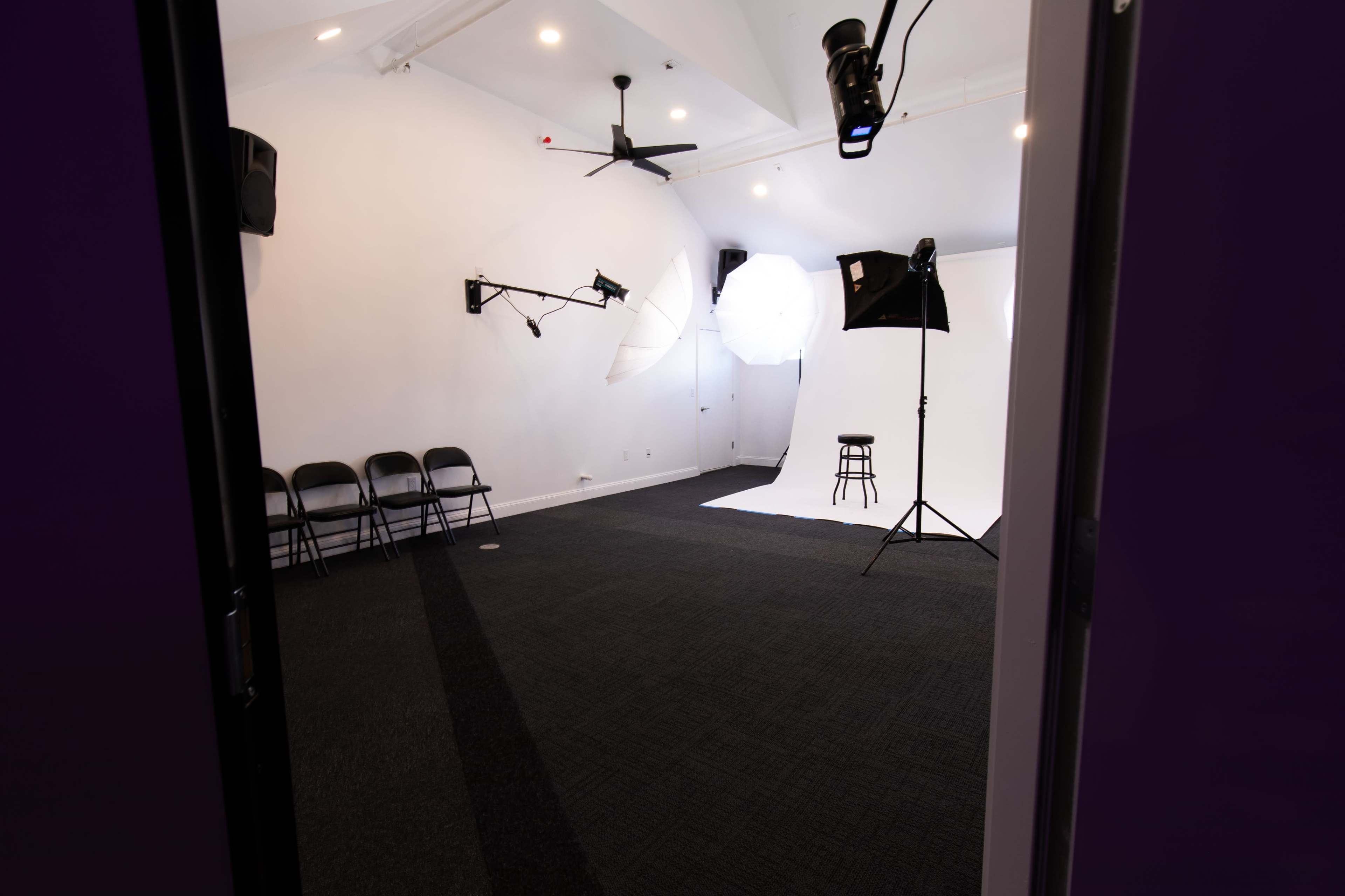 A studio space with chairs arranged along one side, a backdrop set up, and various lighting equipment positioned for a photoshoot.
