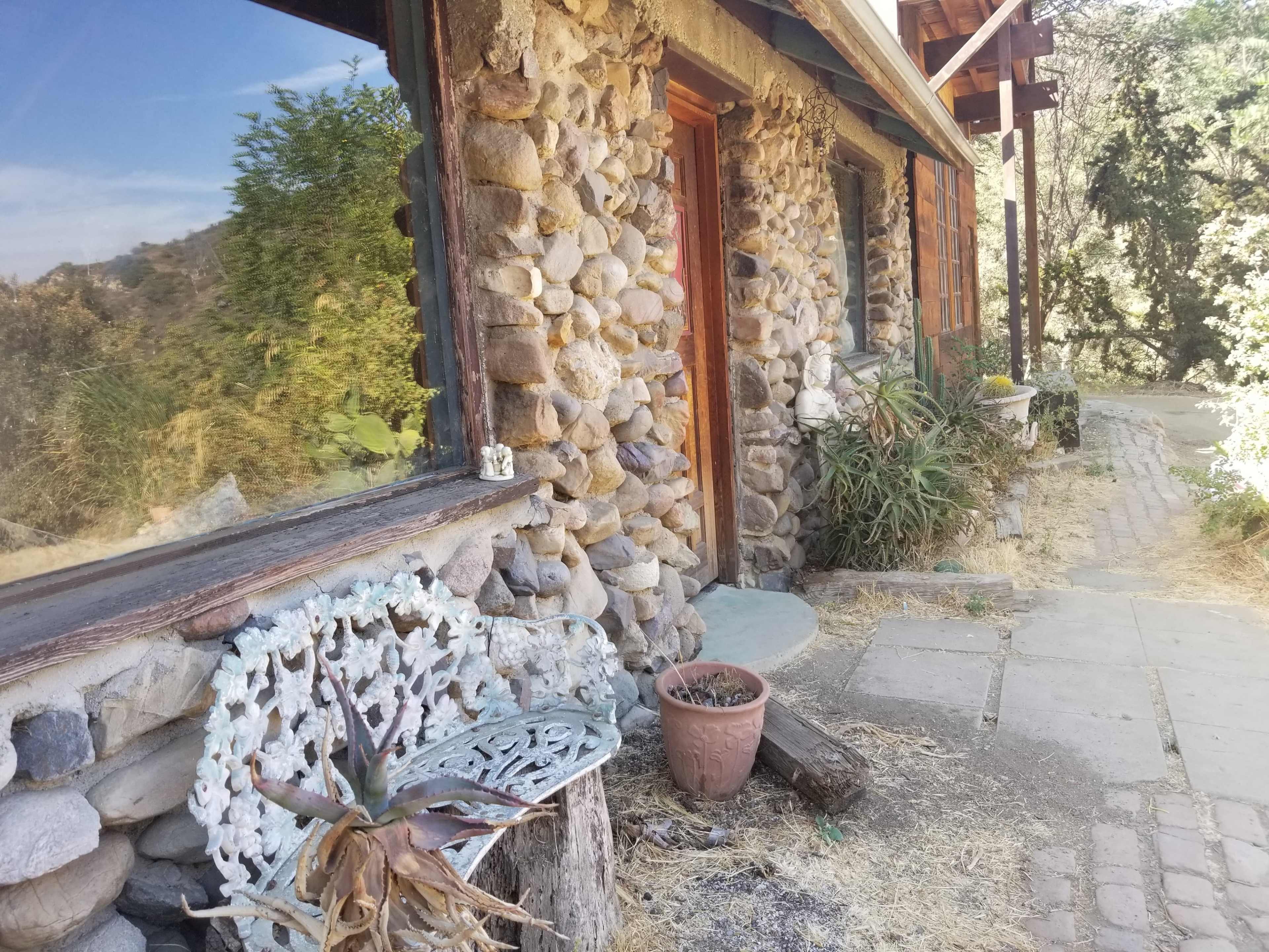 A stone-faced building with wooden doors and a path lined with plants and decorative items.