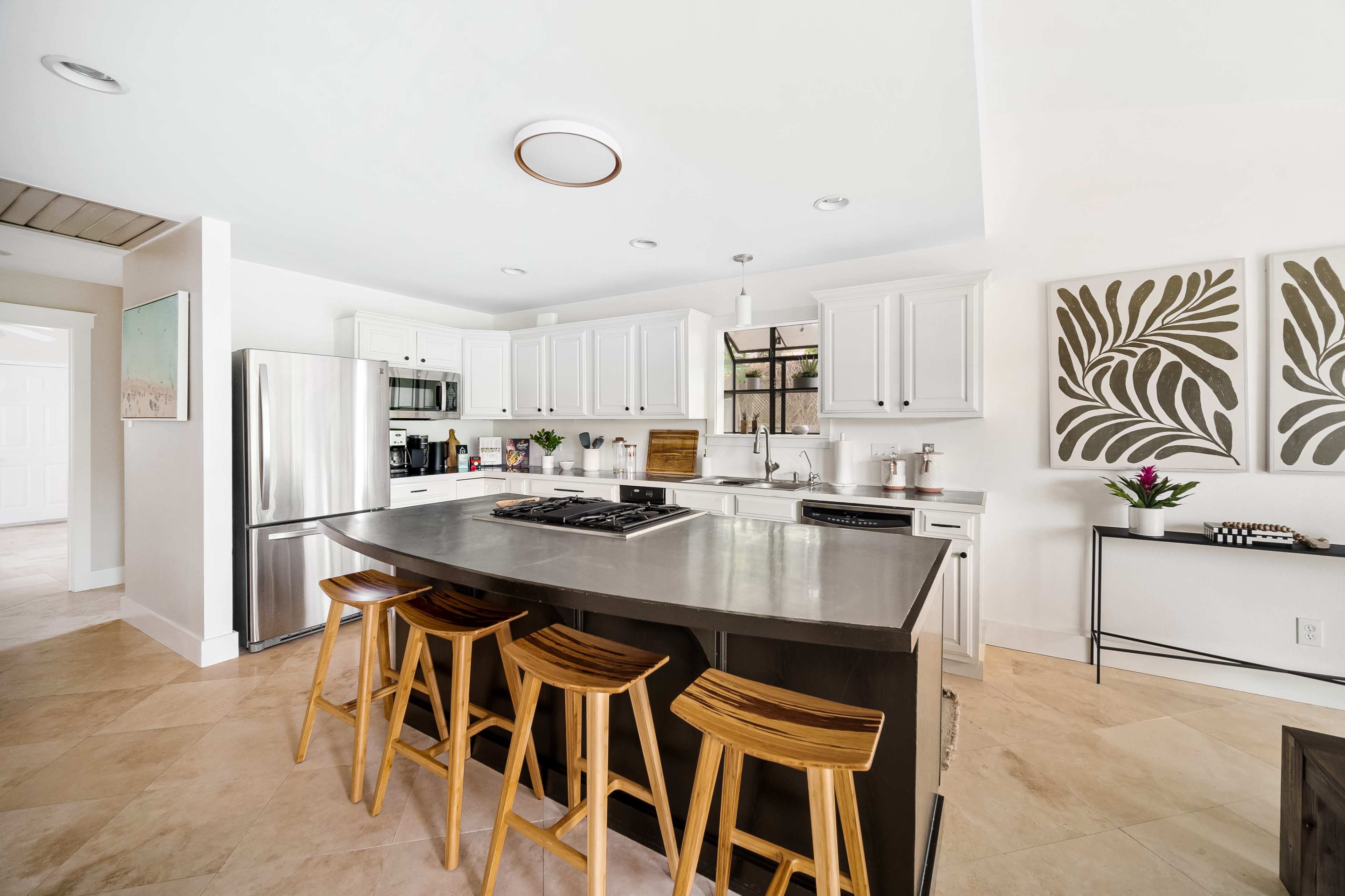 The kitchen features white cabinetry, stainless steel appliances, and a central island with four wooden stools.