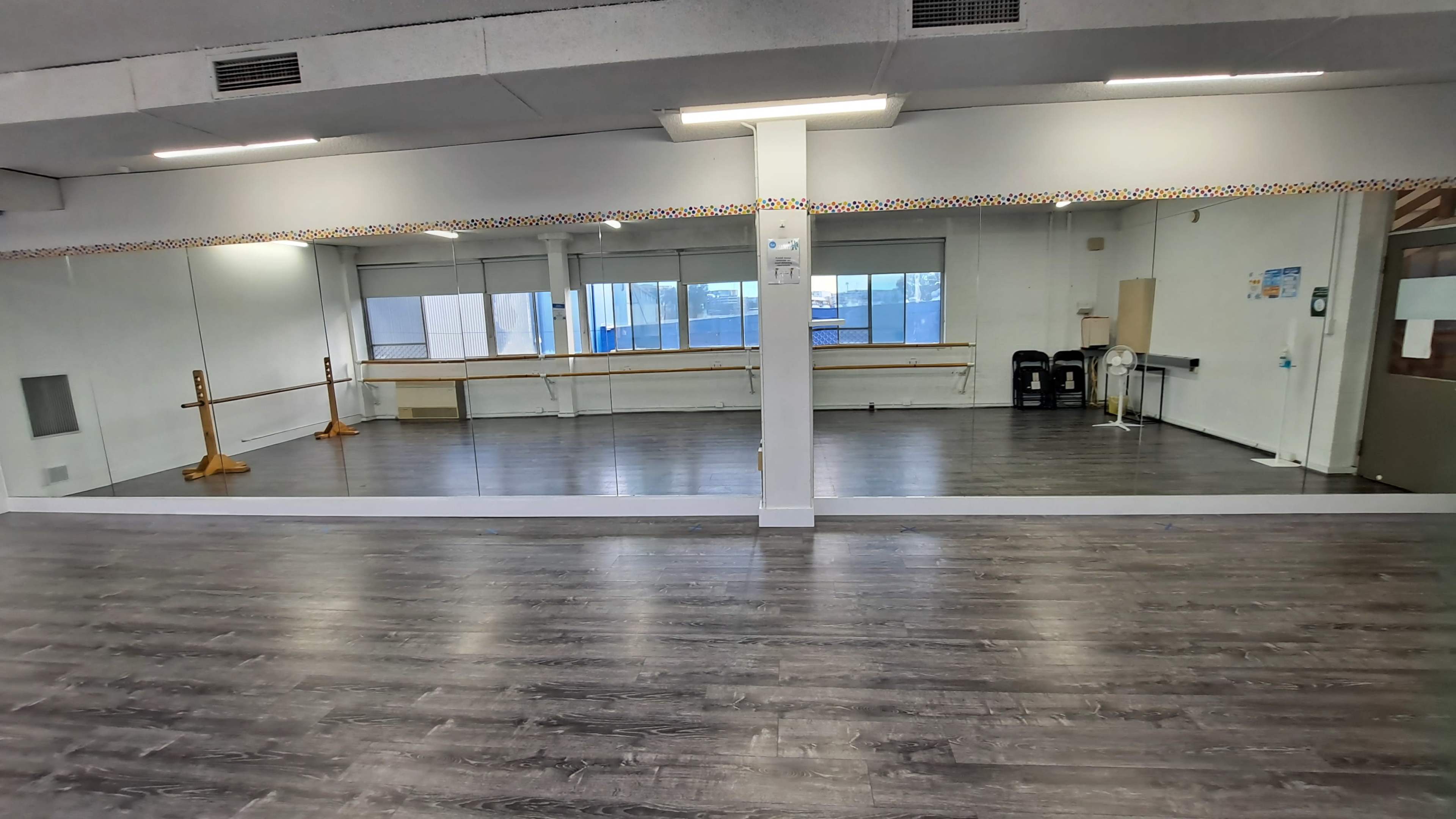 A spacious dance studio with a large mirrored wall, wooden ballet barres, and natural light coming through the windows.