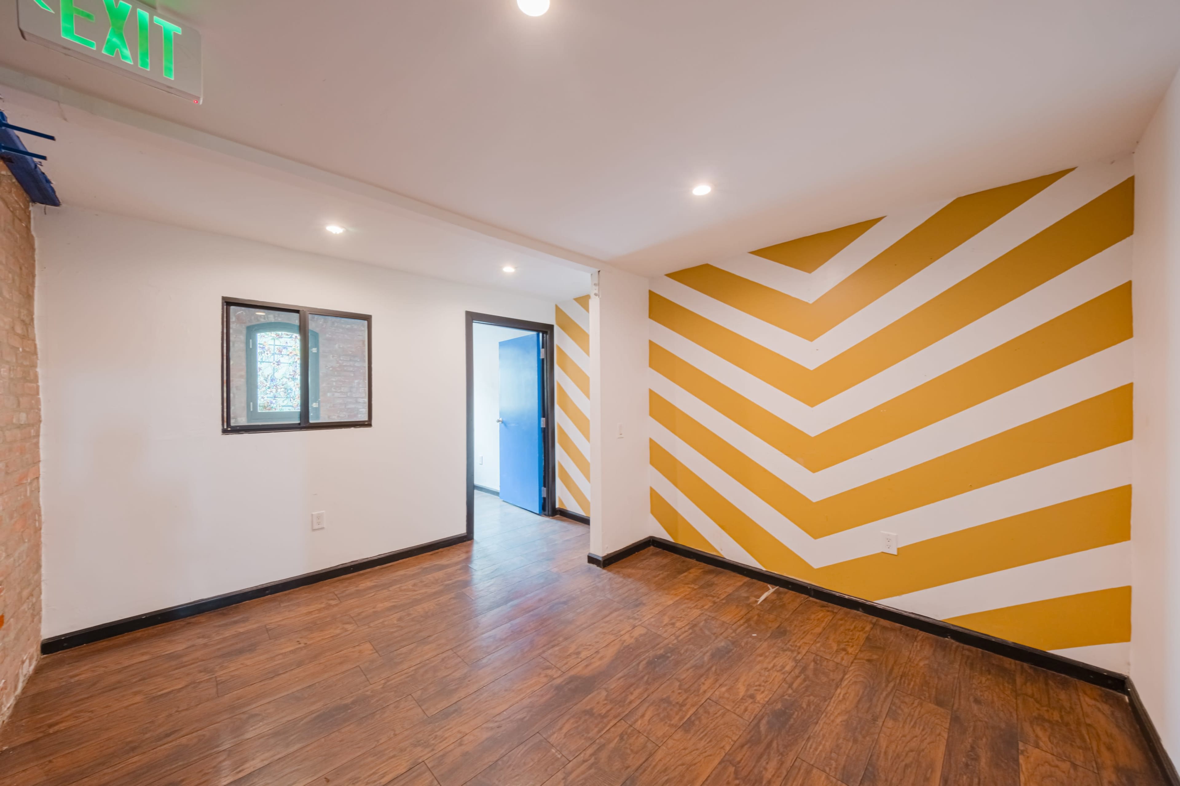 An empty room with a wooden floor, a window on the left wall, and a striped yellow accent wall.