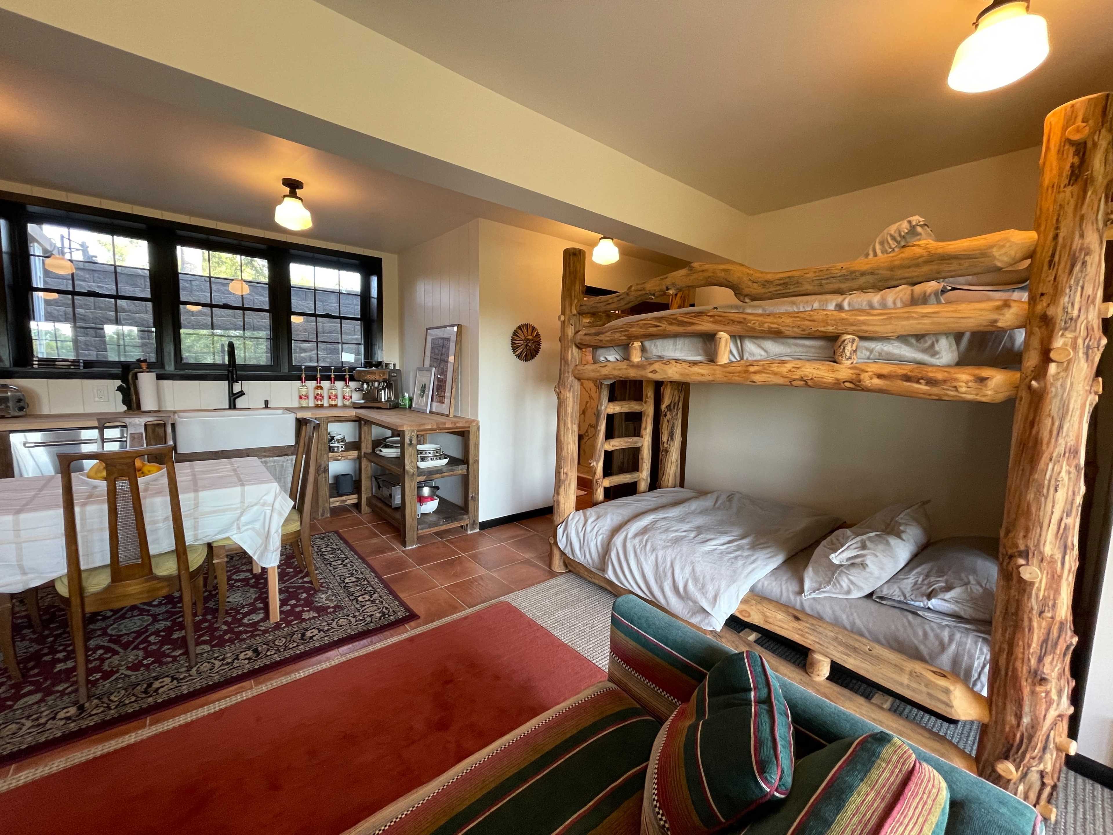 A small, rustic-style living space featuring a bunk bed made of wood, a dining table, and a kitchenette area.