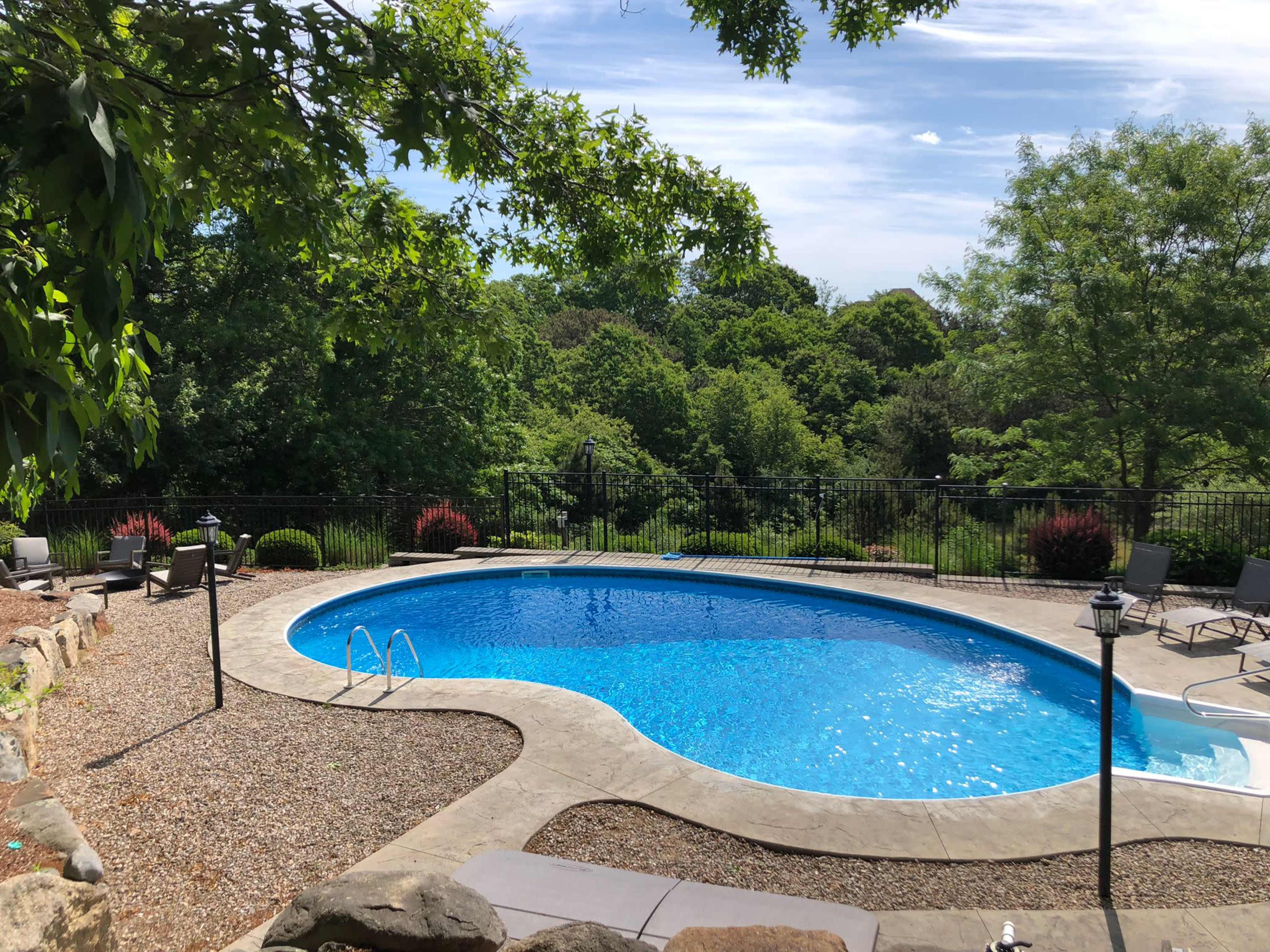 A rectangular swimming pool surrounded by a gravel patio and landscaped greenery.