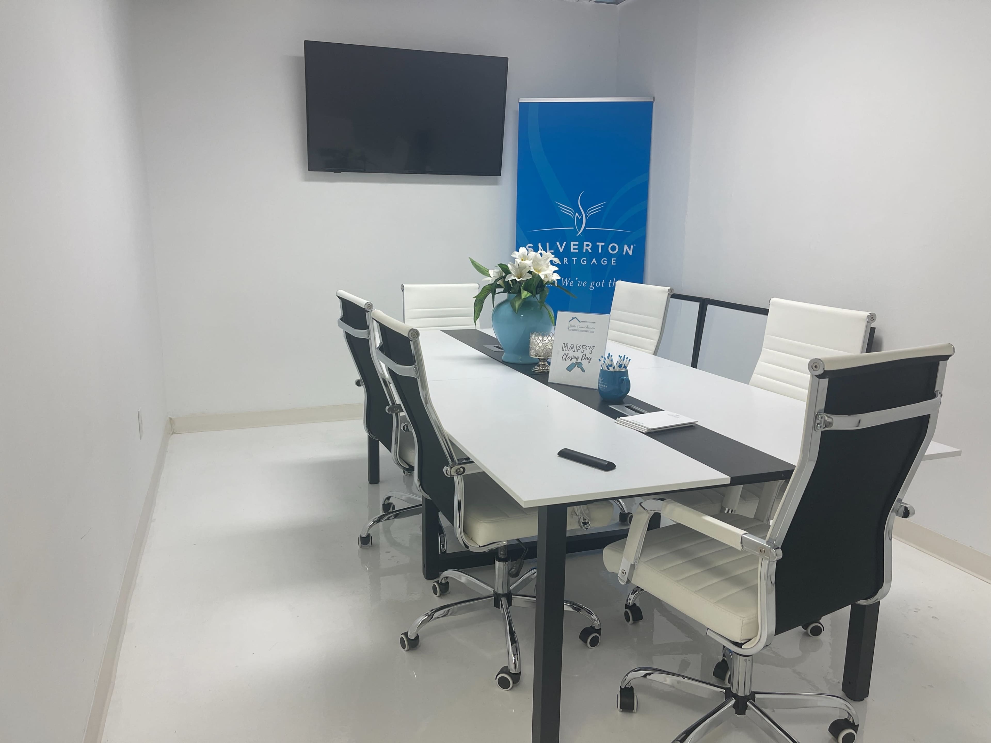 A modern conference room with a large table, white chairs, a TV on the wall, and a banner displaying the name "Silverton Strategy."
