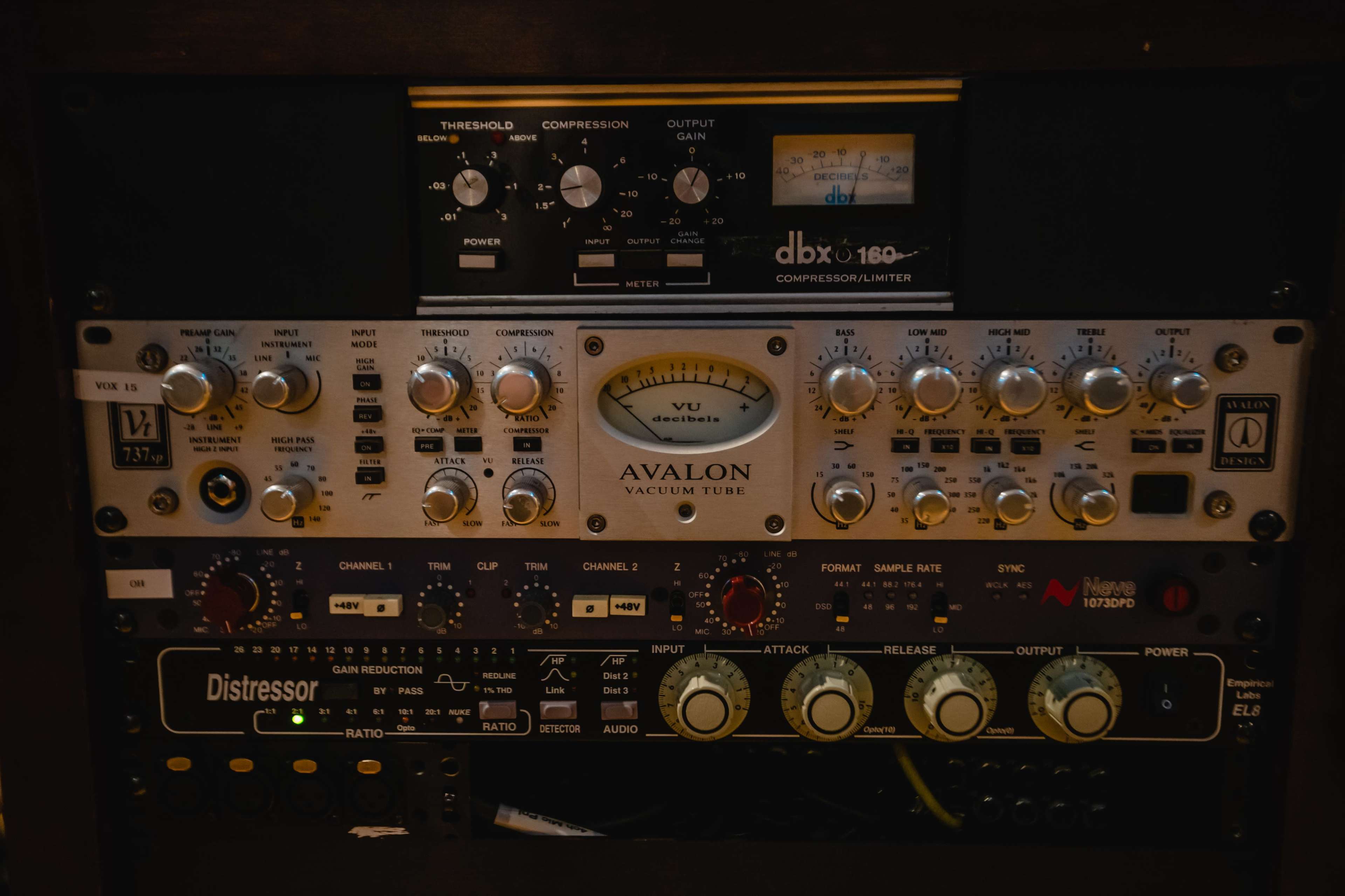 A rack-mounted audio equipment setup featuring a DBX 160 compressor, an Avalon vacuum tube preamp, and an Empirical Labs Distressor, each with various knobs and settings.