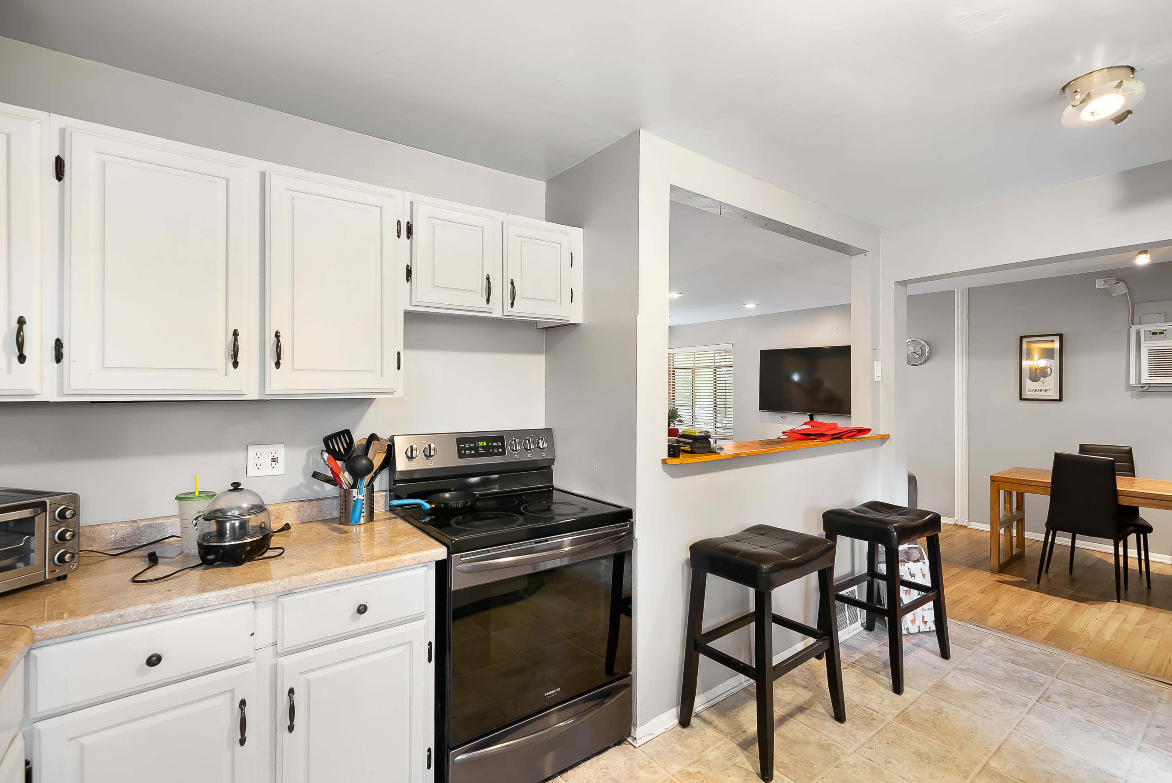 The image shows a kitchen area with white cabinetry, a black stove, and a small dining space visible in the background.