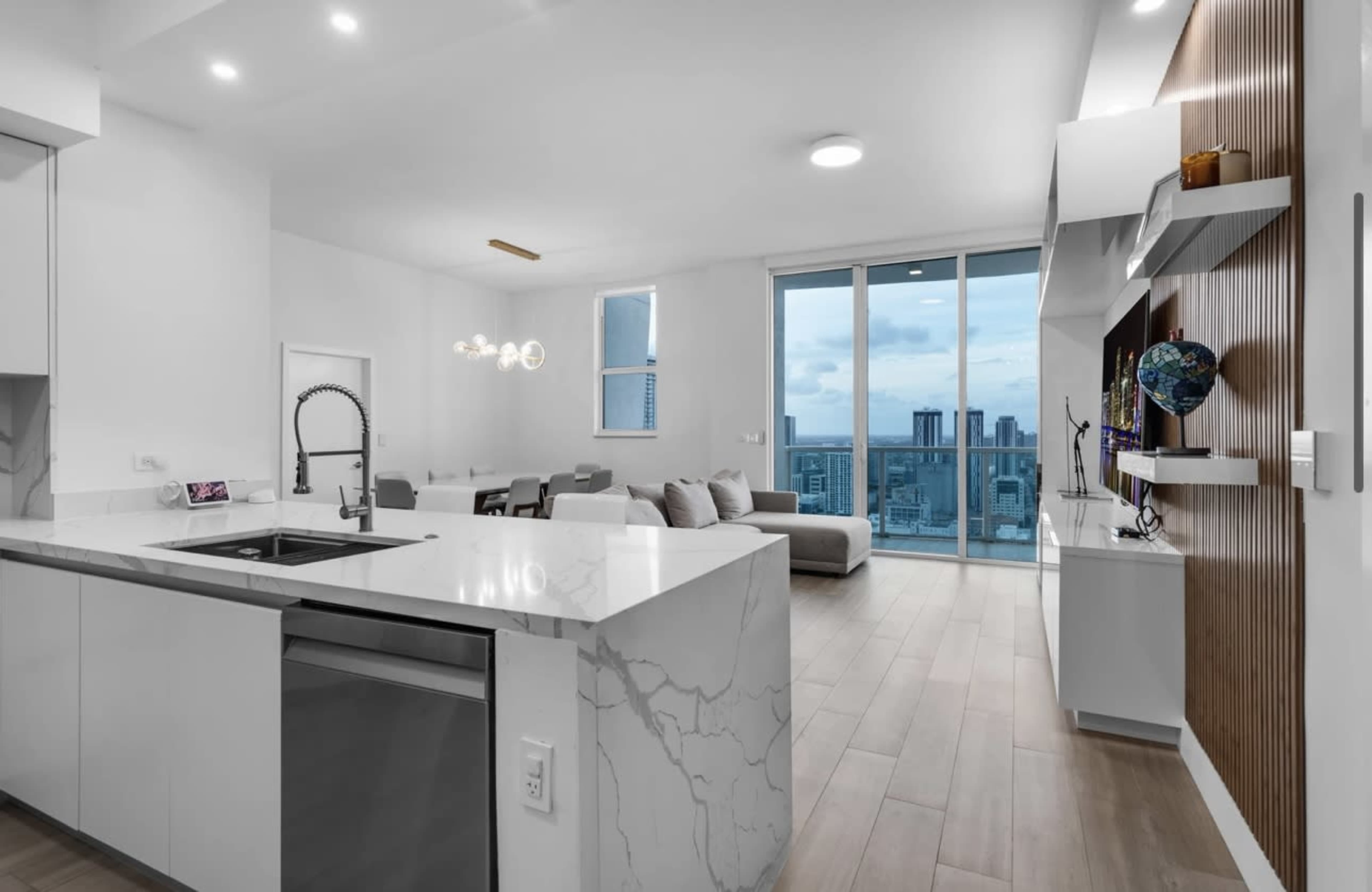 A modern kitchen opens to a living area with a large window overlooking a city skyline.