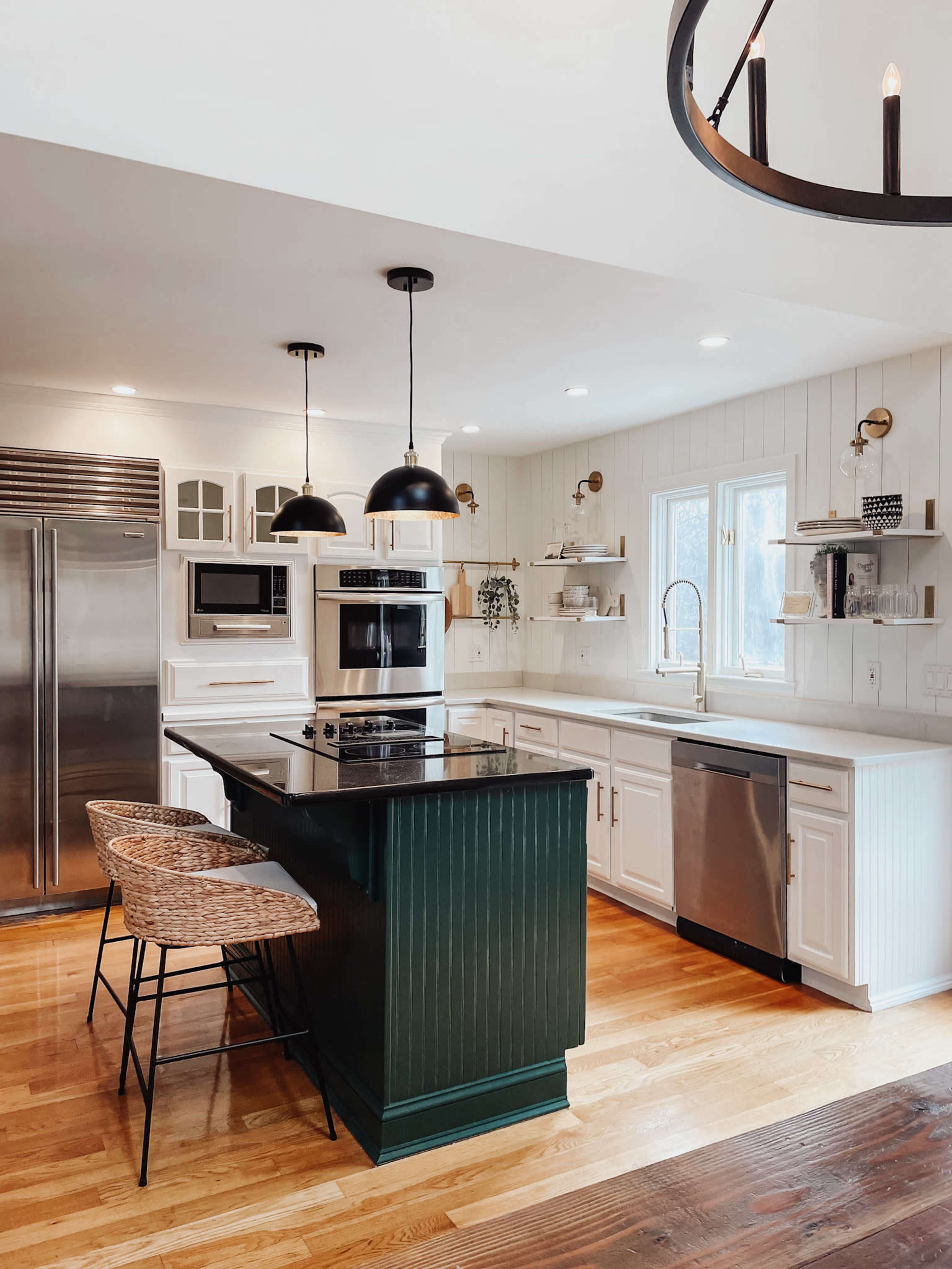 A modern kitchen features a central island with a dark green base, two bar stools, stainless steel appliances, and white cabinetry with wooden accents.