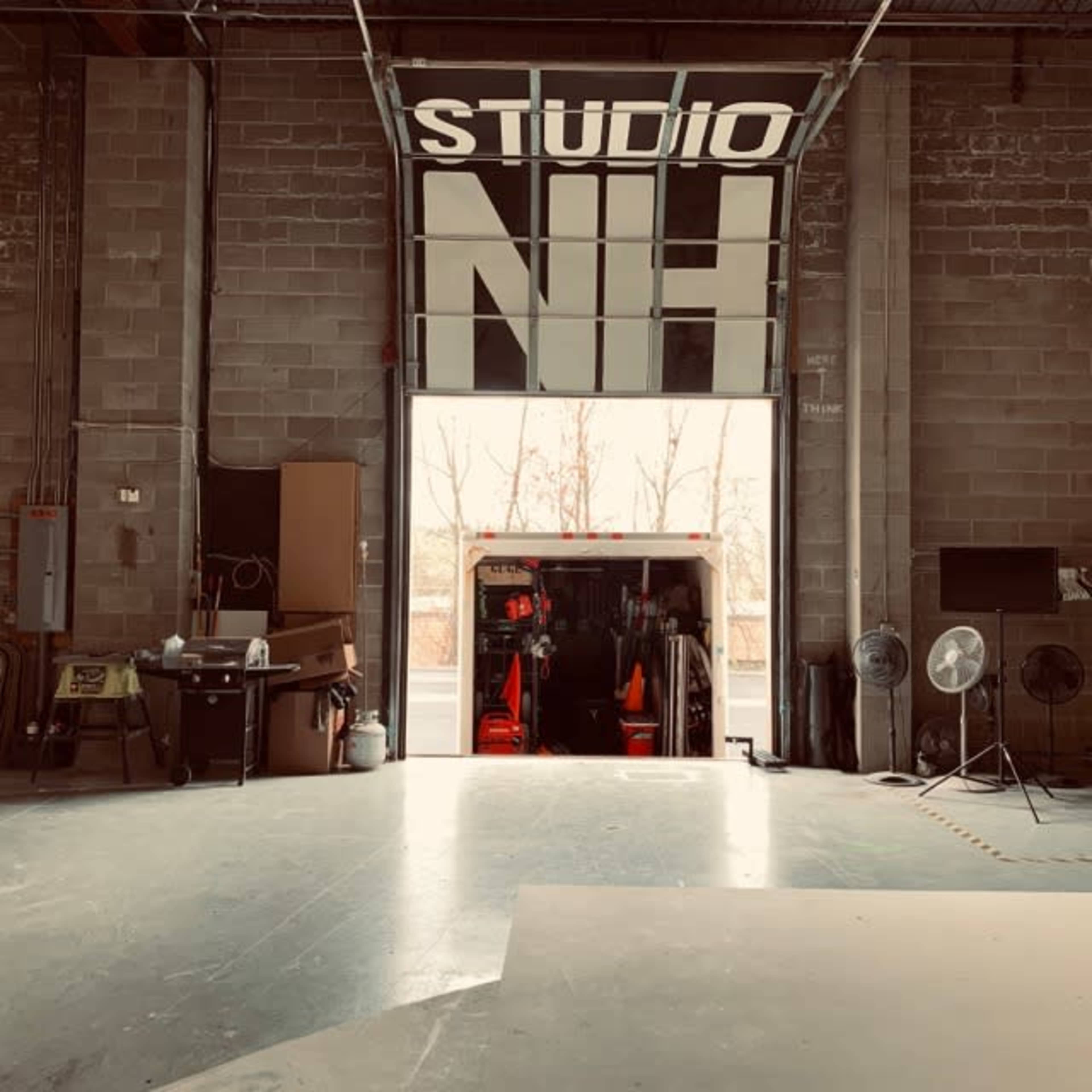 An industrial space with an open garage door revealing a truck filled with equipment, and the words "STUDIO NH" prominently displayed above.