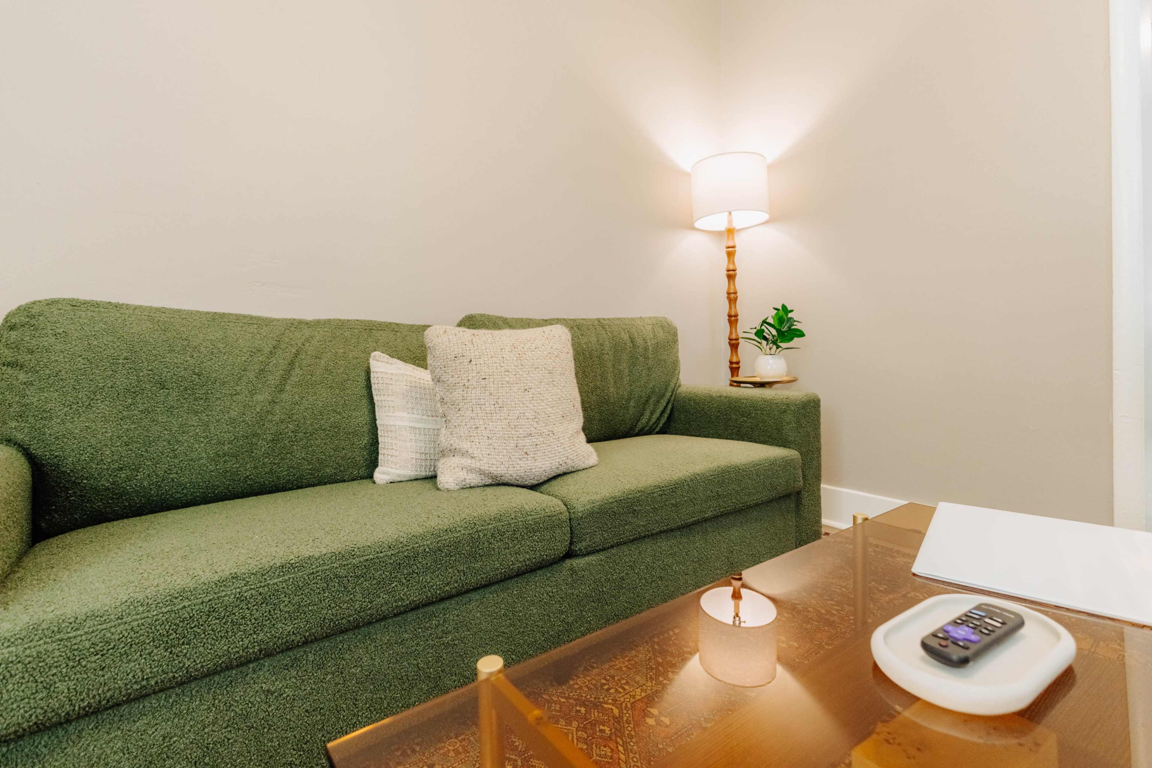 A green sofa with a decorative pillow is positioned near a lamp and a small potted plant on a side table.