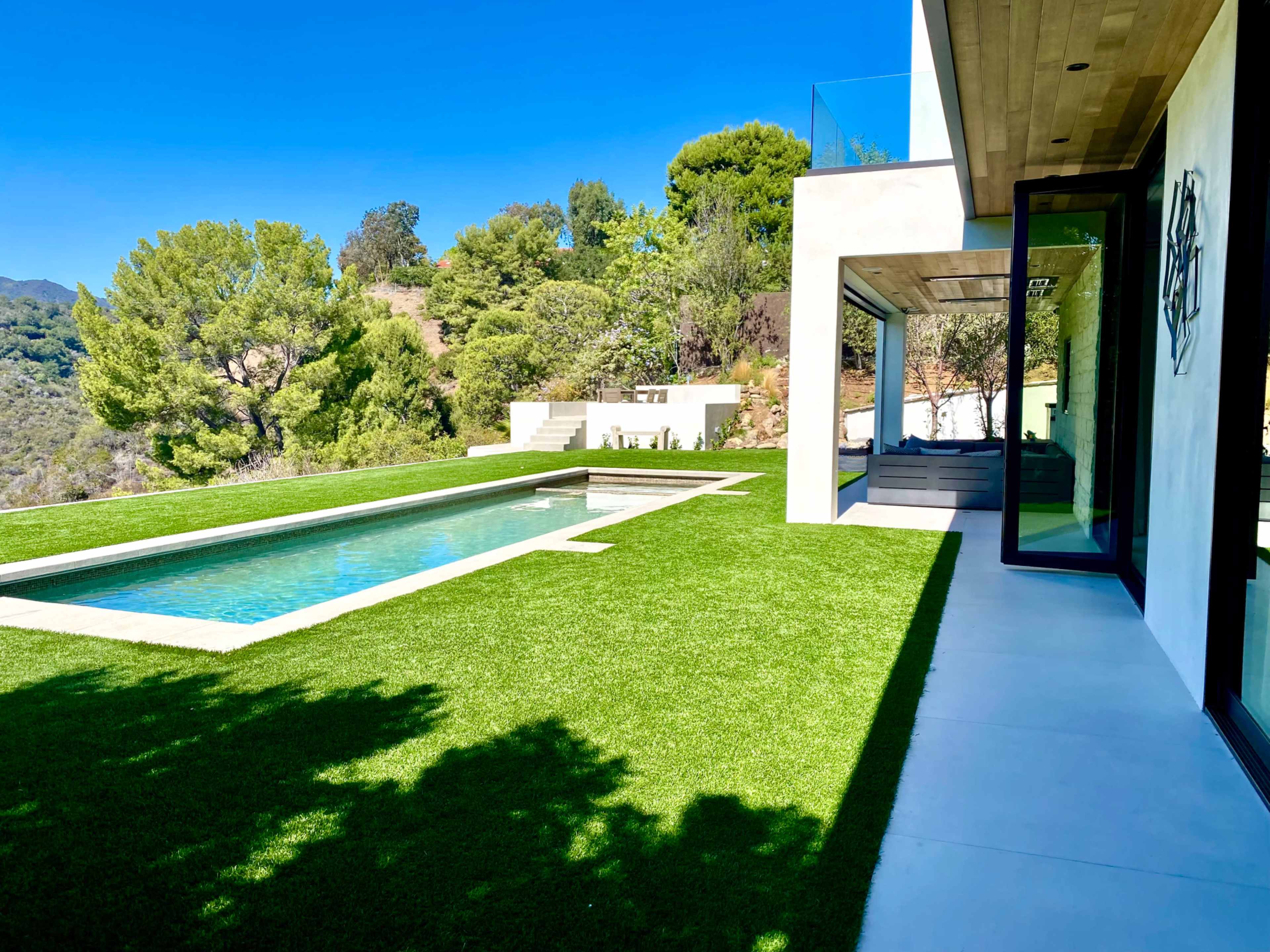 A modern home with a pool surrounded by neatly manicured grass and greenery in the background.