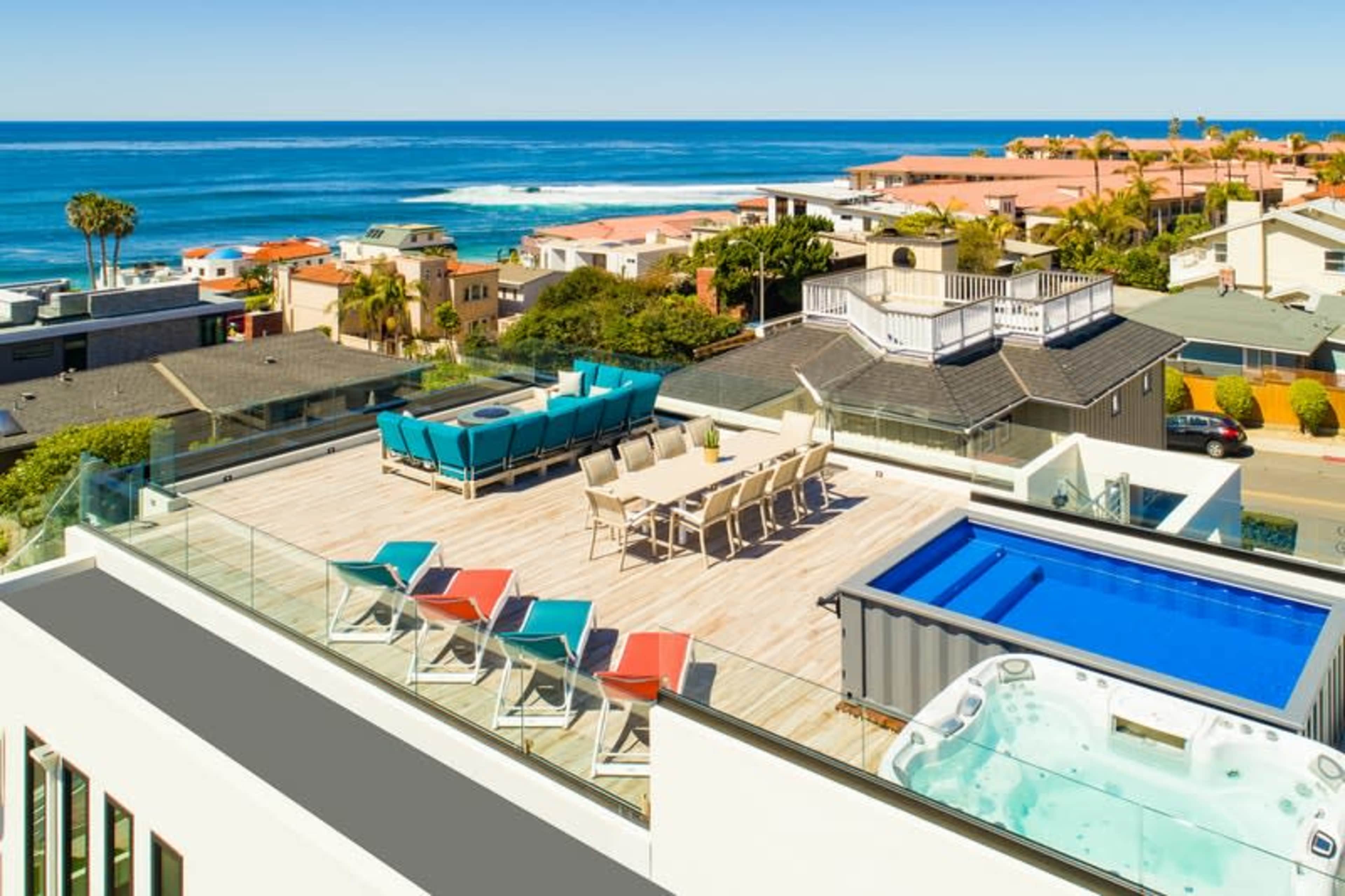 The rooftop features a large dining area, a swimming pool, a hot tub, and several lounge chairs overlooking the ocean.