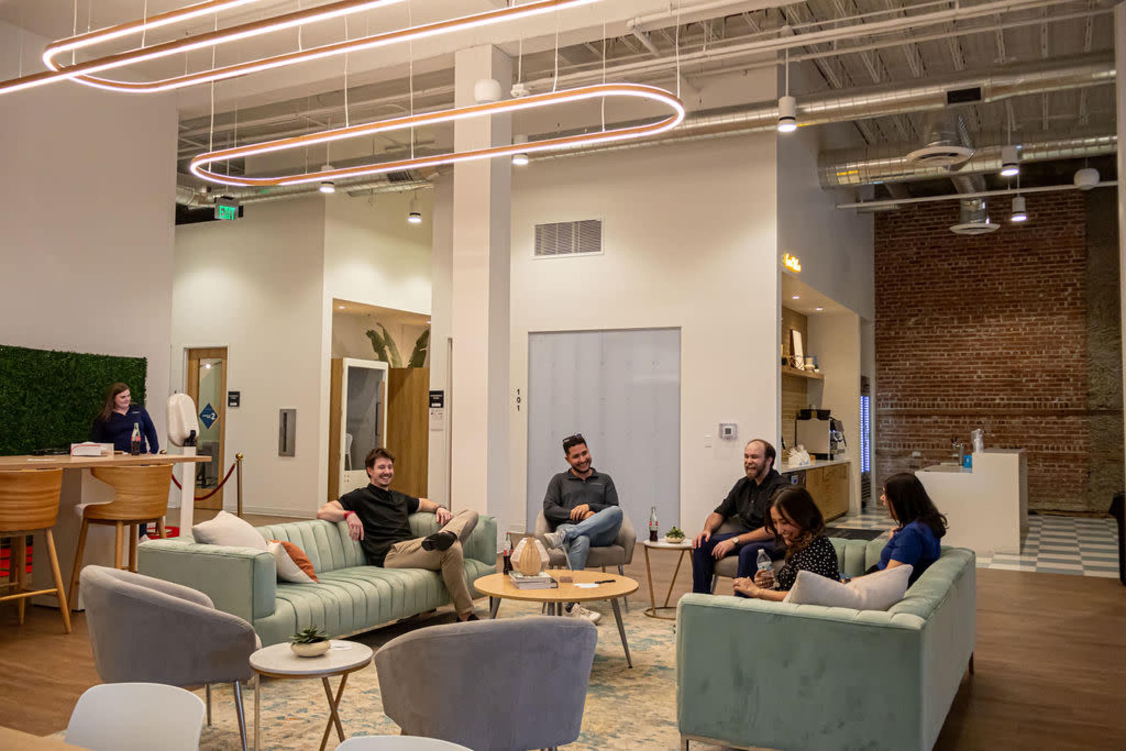 A group of five people relaxes in a modern lounge area with light-colored couches and a tall moss wall in a well-lit space.