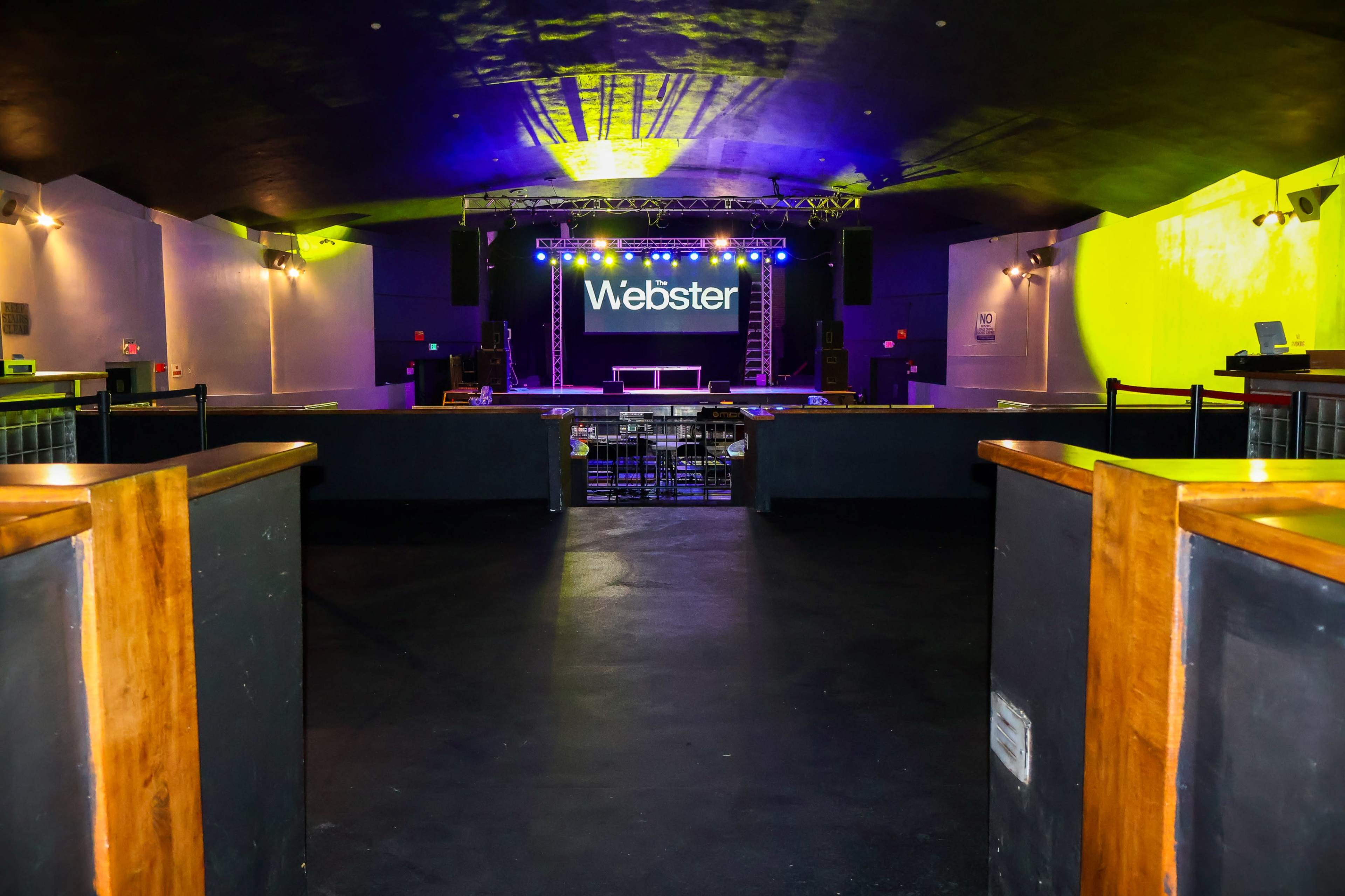An empty nightclub with a stage displaying the name "Webster" illuminated in bright lights.