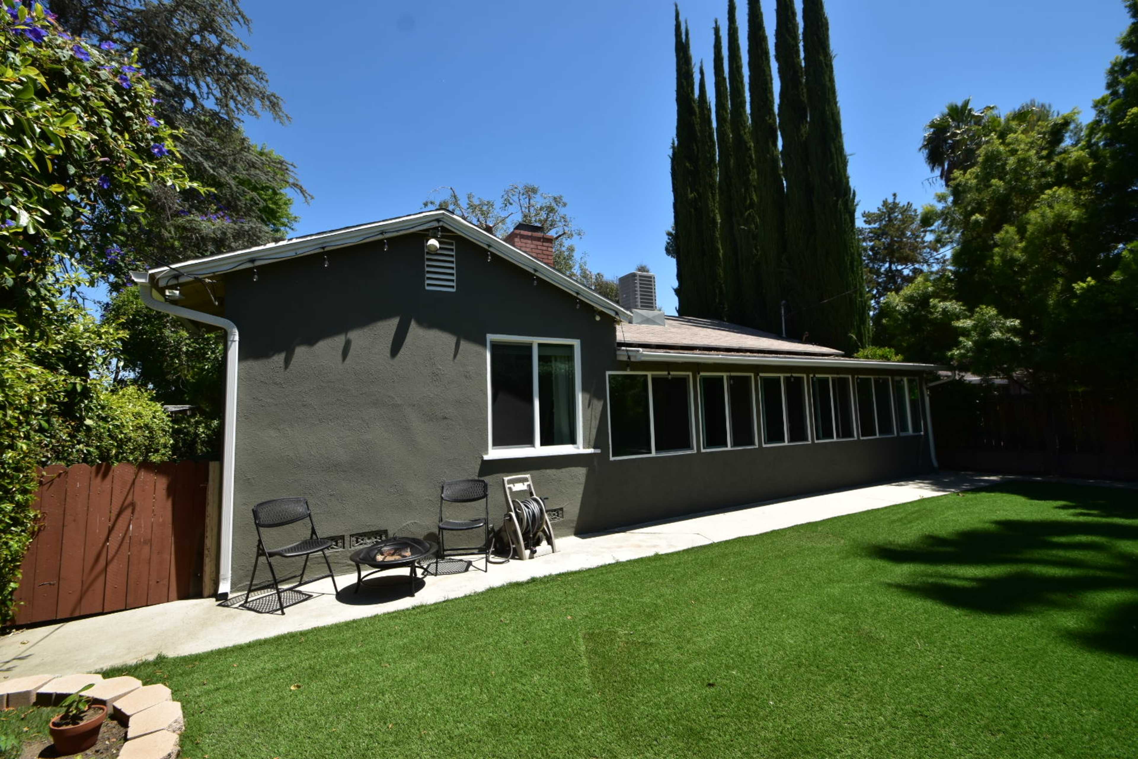 A gray house with large windows sits next to a well-maintained lawn and tall trees in the background.