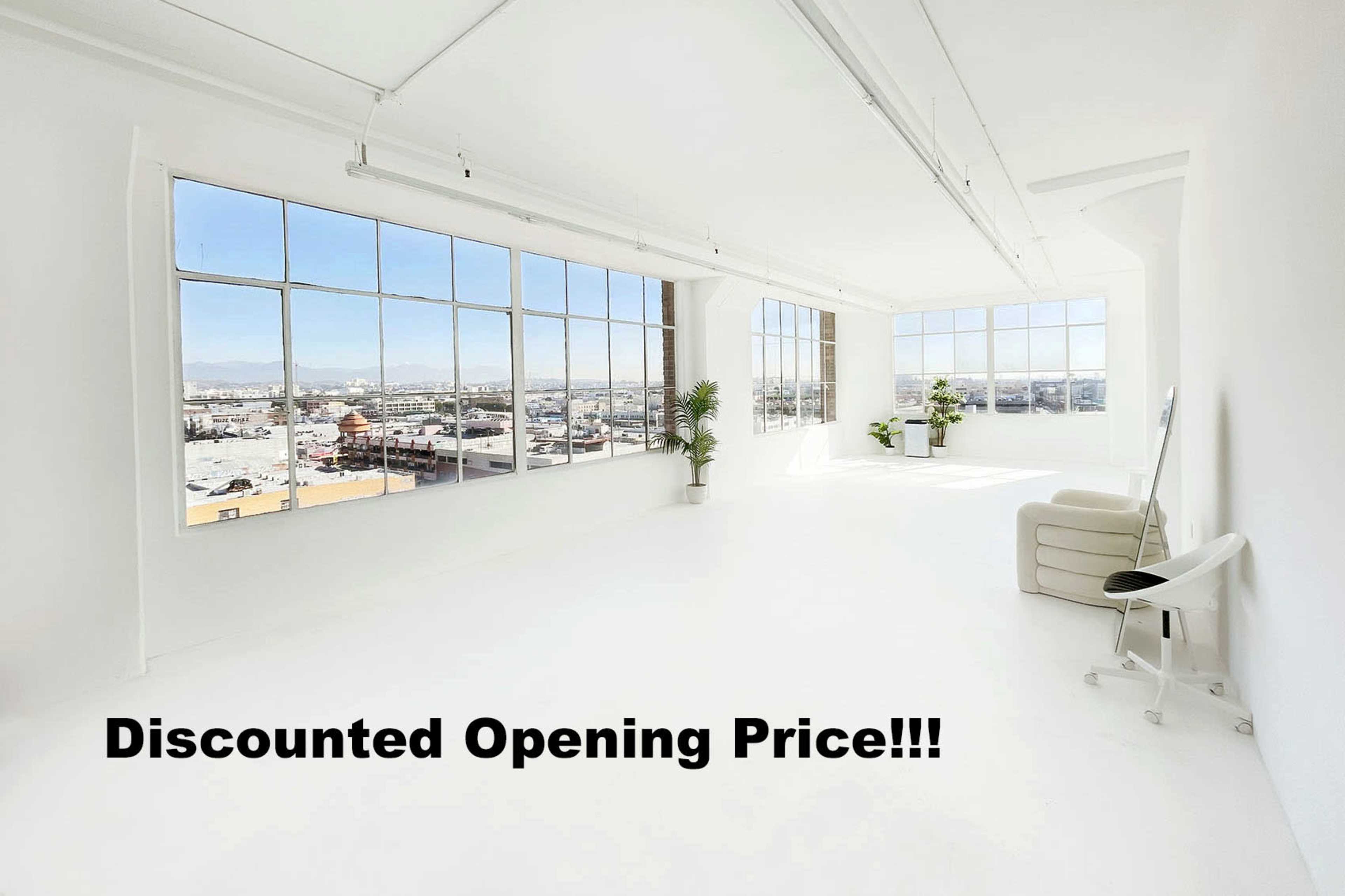 A bright, spacious room with large windows overlooking a cityscape, featuring minimalist furniture and greenery.